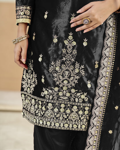 Black embroidered garment with gold detailing on a neutral background