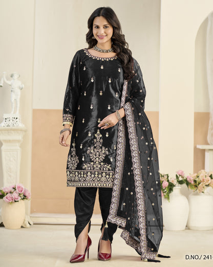 Woman wearing a black embroidered traditional outfit with a sheer dupatta in a decorated room.