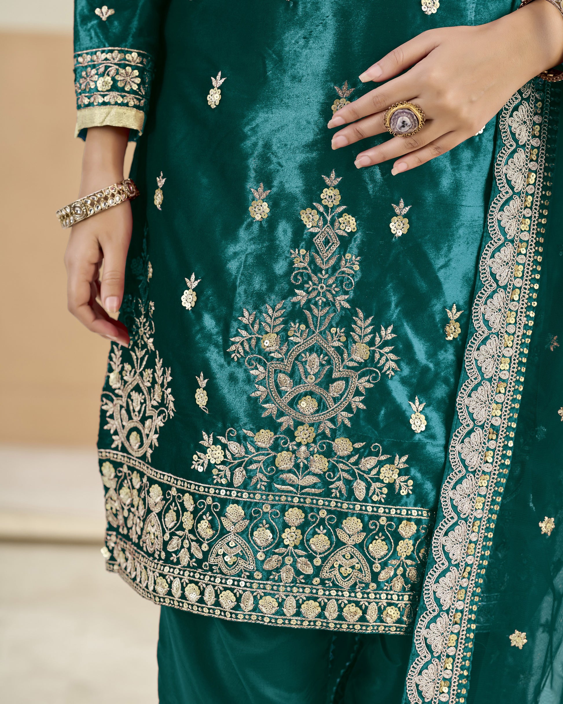 Close-up of a green embroidered garment with intricate patterns and jewelry.
