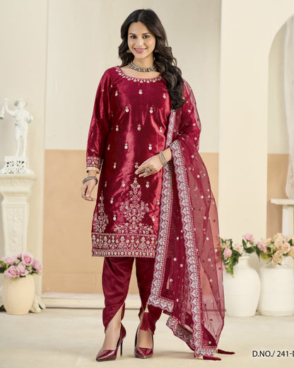 Woman wearing a maroon traditional outfit with white embroidery in a decorated room.