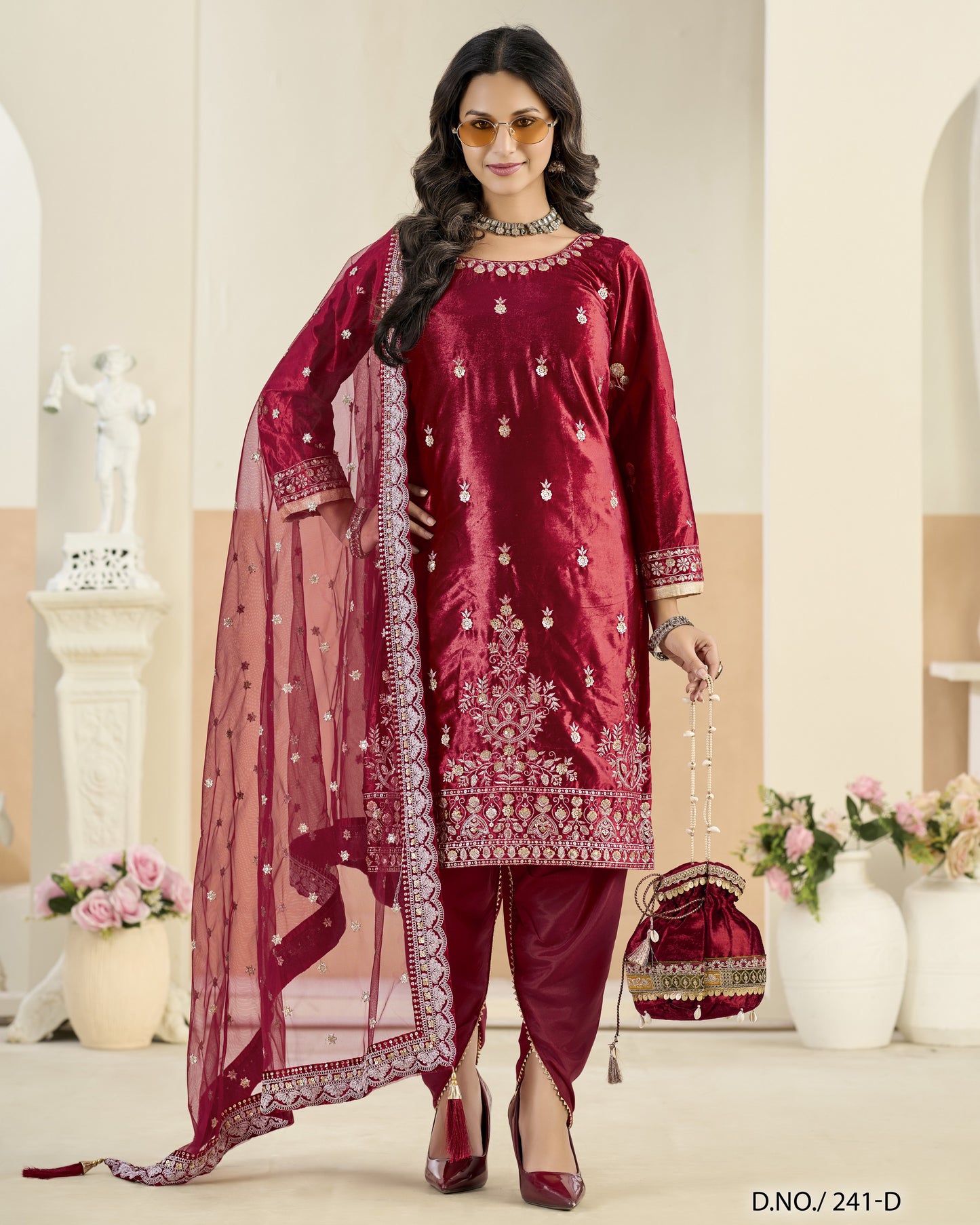 Woman in a red embroidered traditional outfit with a dupatta, standing in a decorated room.
