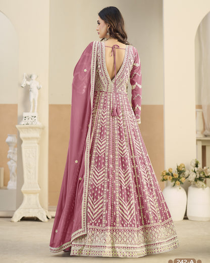 Woman wearing a pink and white embroidered traditional outfit in a decorated room.