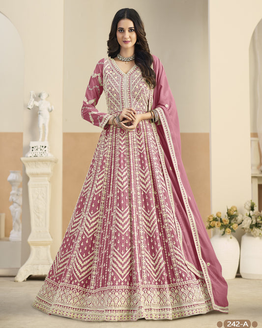 Woman wearing a traditional pink and white embroidered anarkali suit in a decorated room.