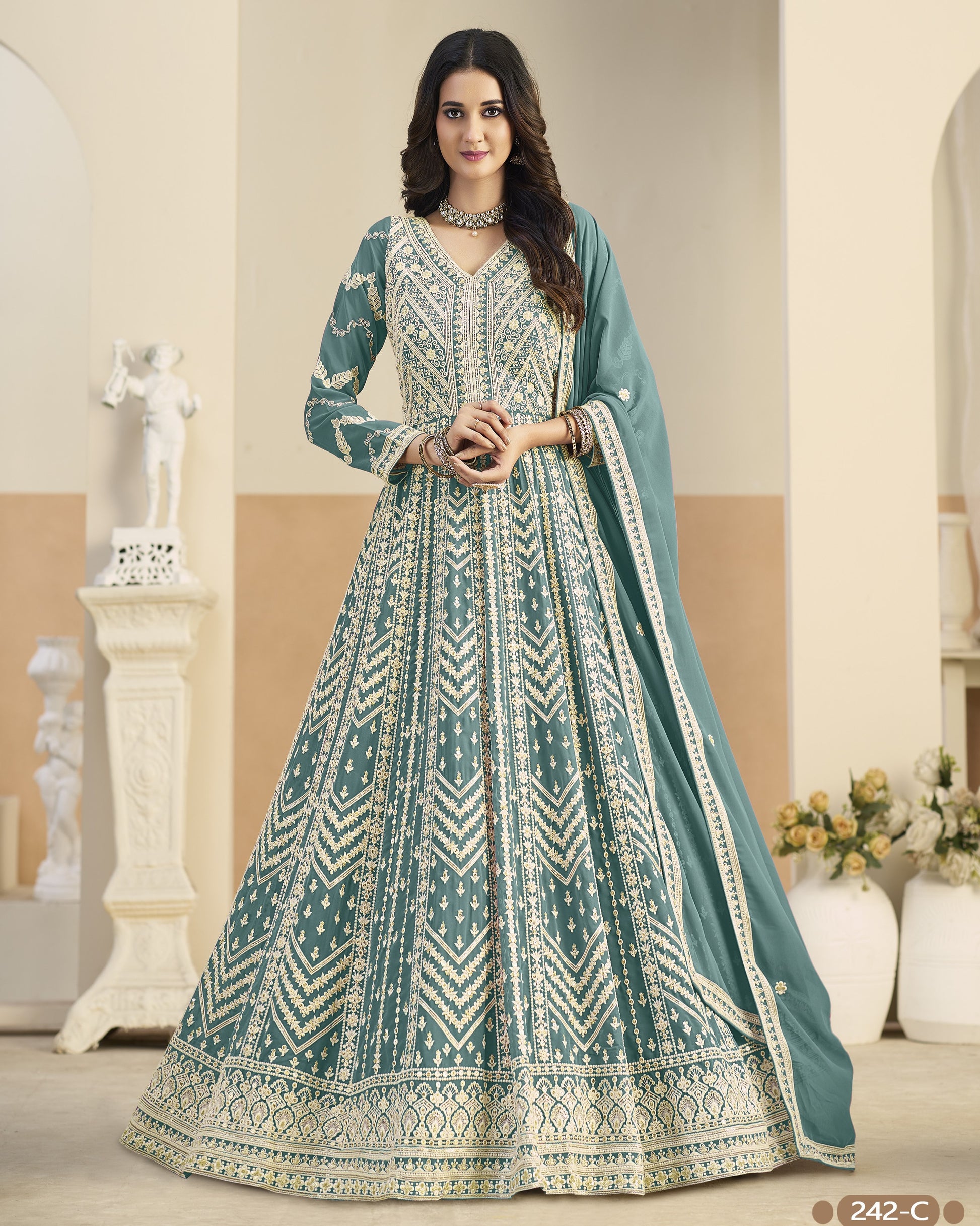 Woman wearing a traditional teal and white embroidered dress in an elegant indoor setting.