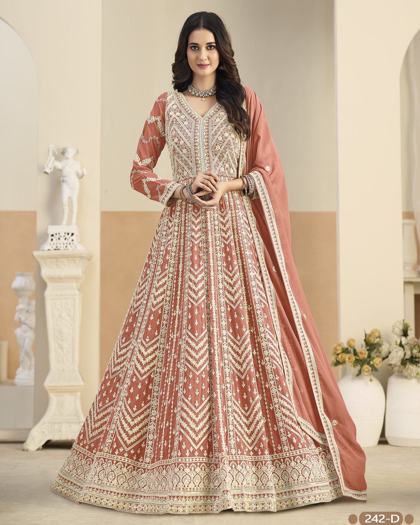 Woman wearing a traditional embroidered dress with a dupatta in a decorated room.