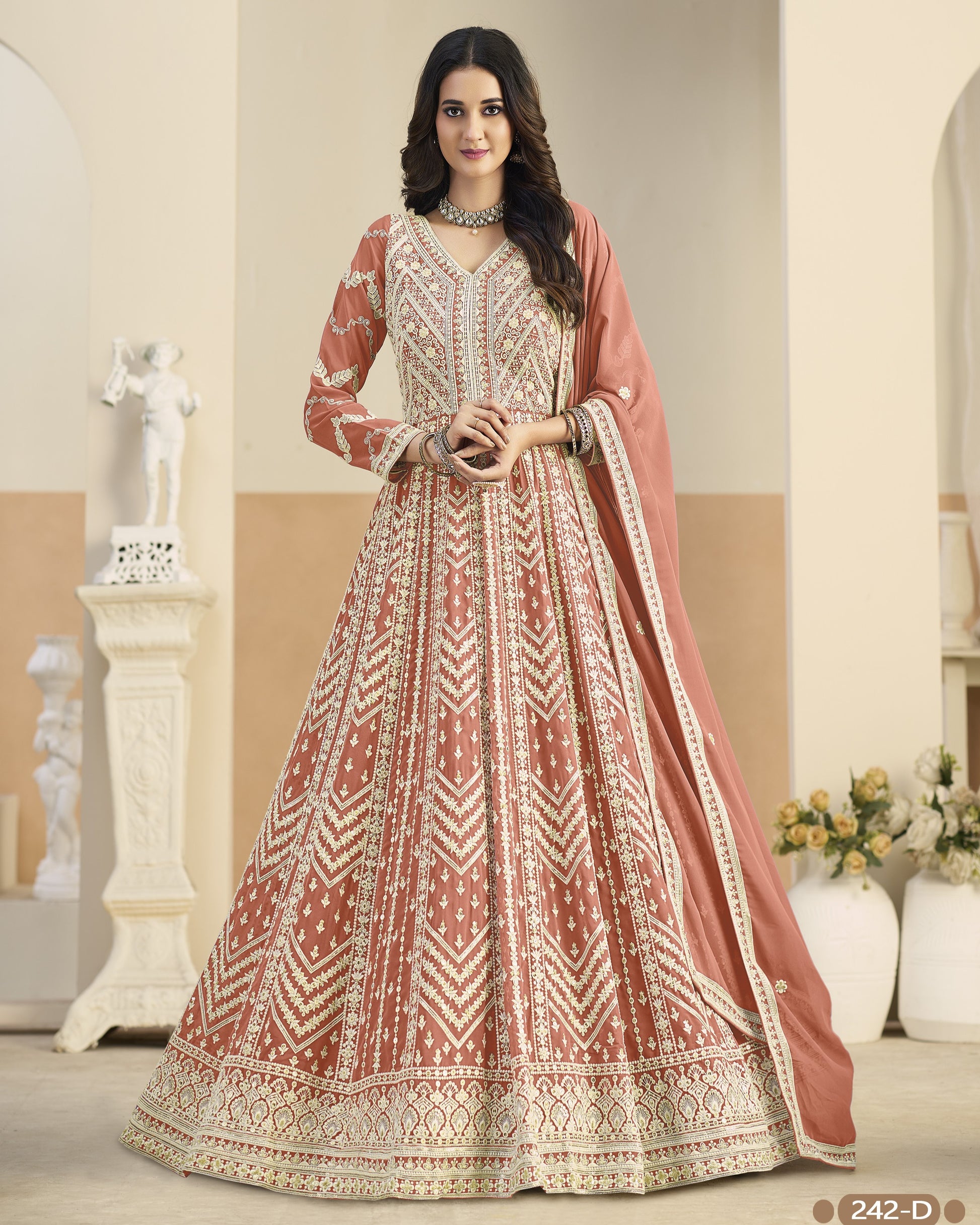 Woman wearing a traditional embroidered dress with a dupatta in a decorated room.