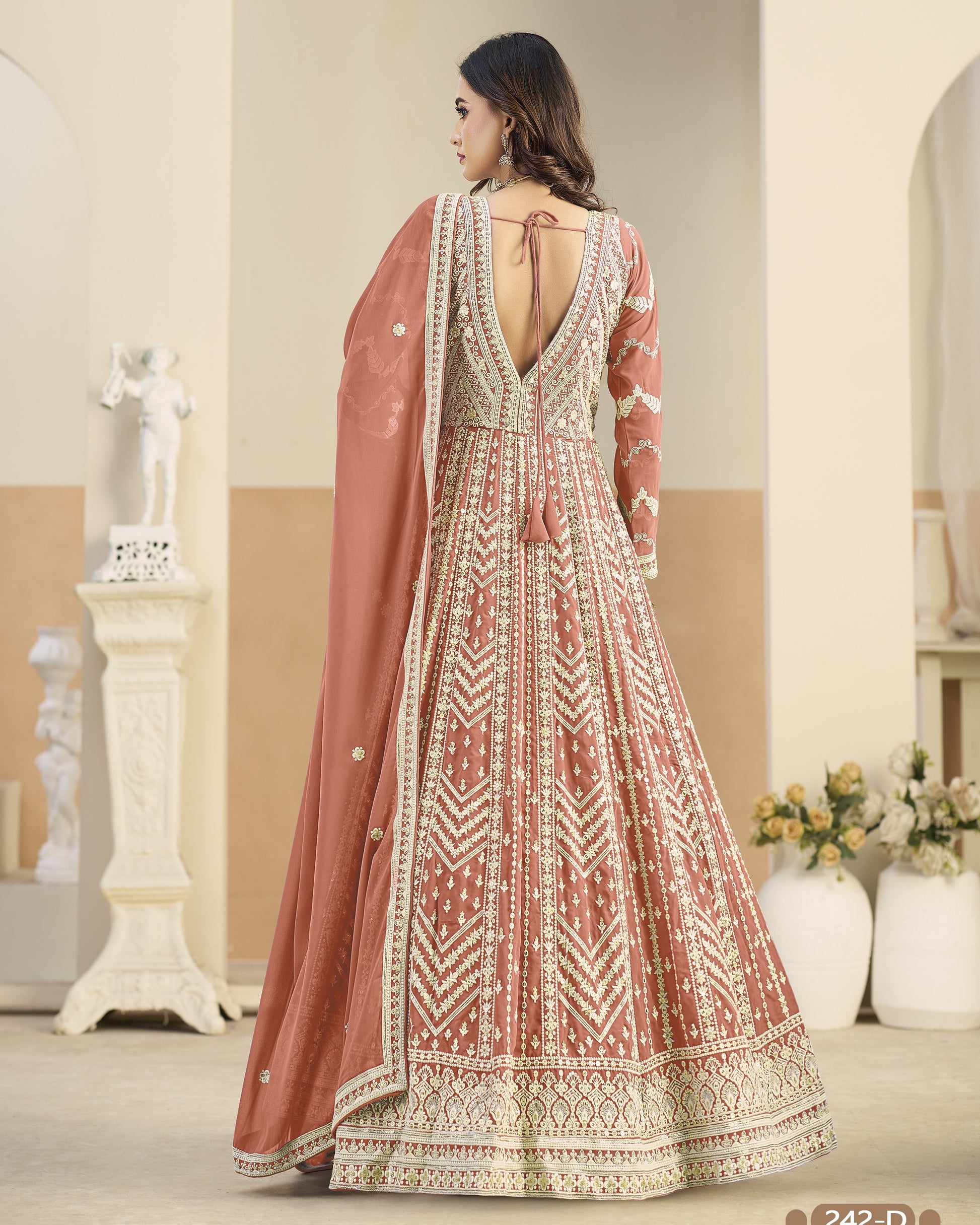 Woman wearing a traditional embroidered dress with a pink dupatta in an indoor setting.