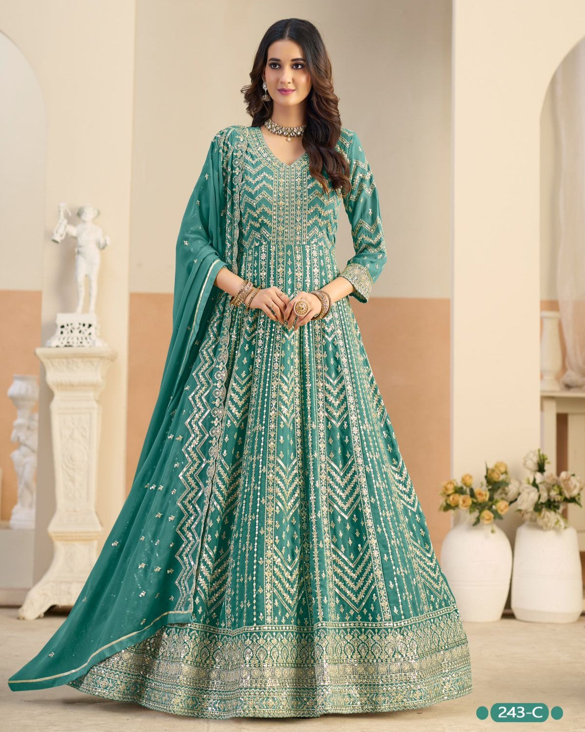 Woman wearing a teal embroidered anarkali suit in a decorated room.