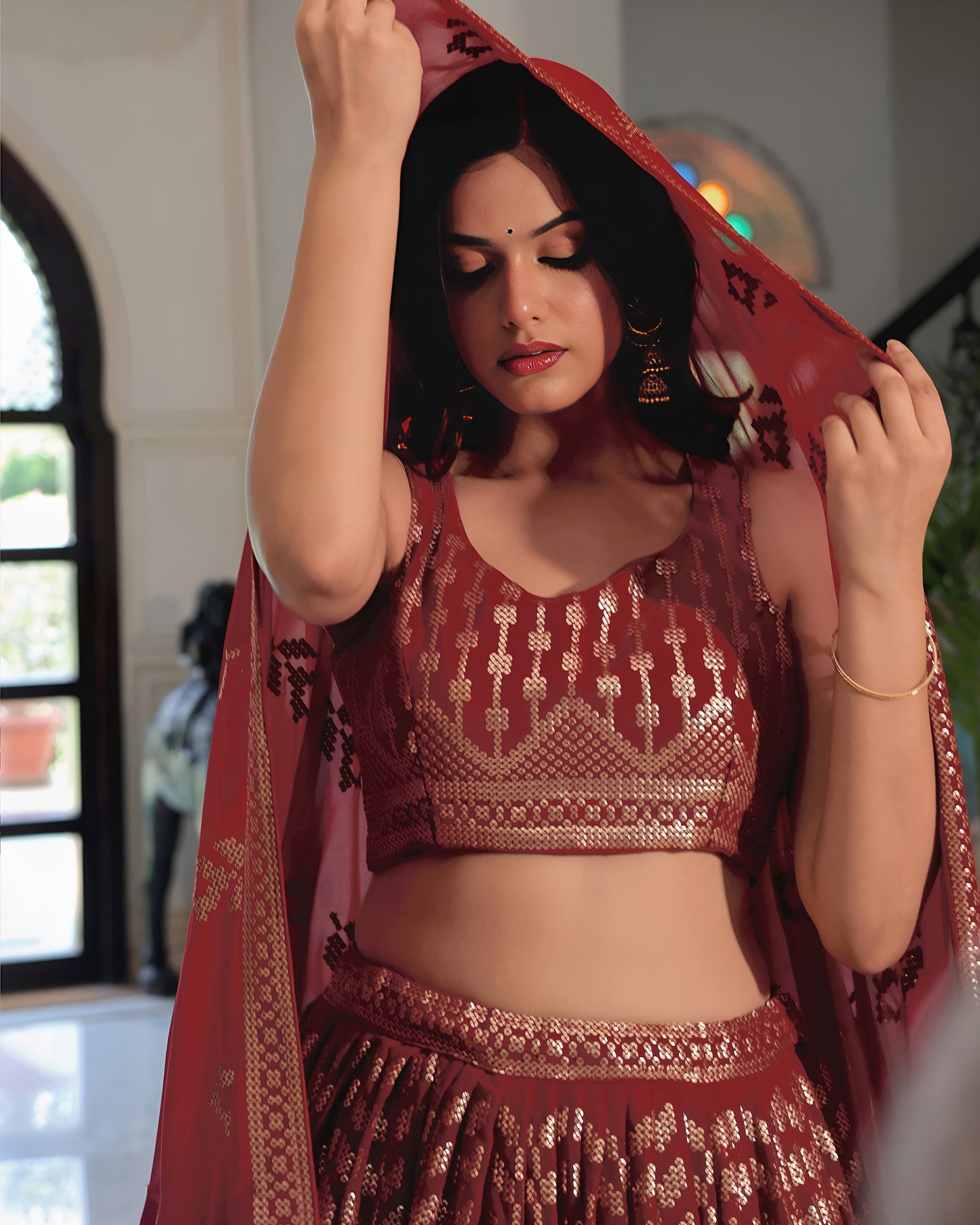 Woman in traditional red and gold outfit with a patterned dupatta indoors.