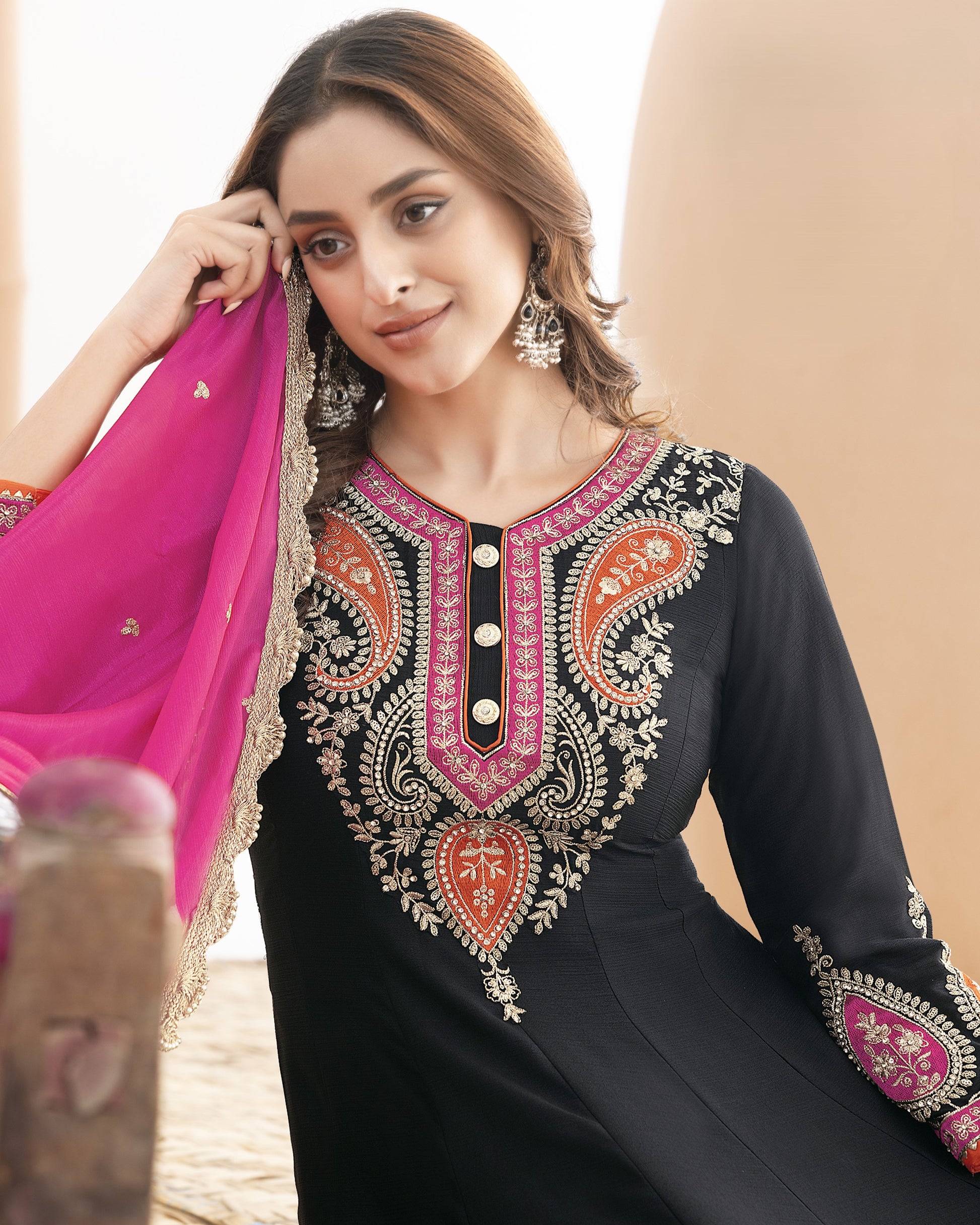 Woman wearing a black embroidered dress with pink and gold details, holding a pink dupatta.