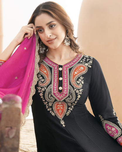 Woman wearing a black embroidered dress with pink and gold details, holding a pink dupatta.