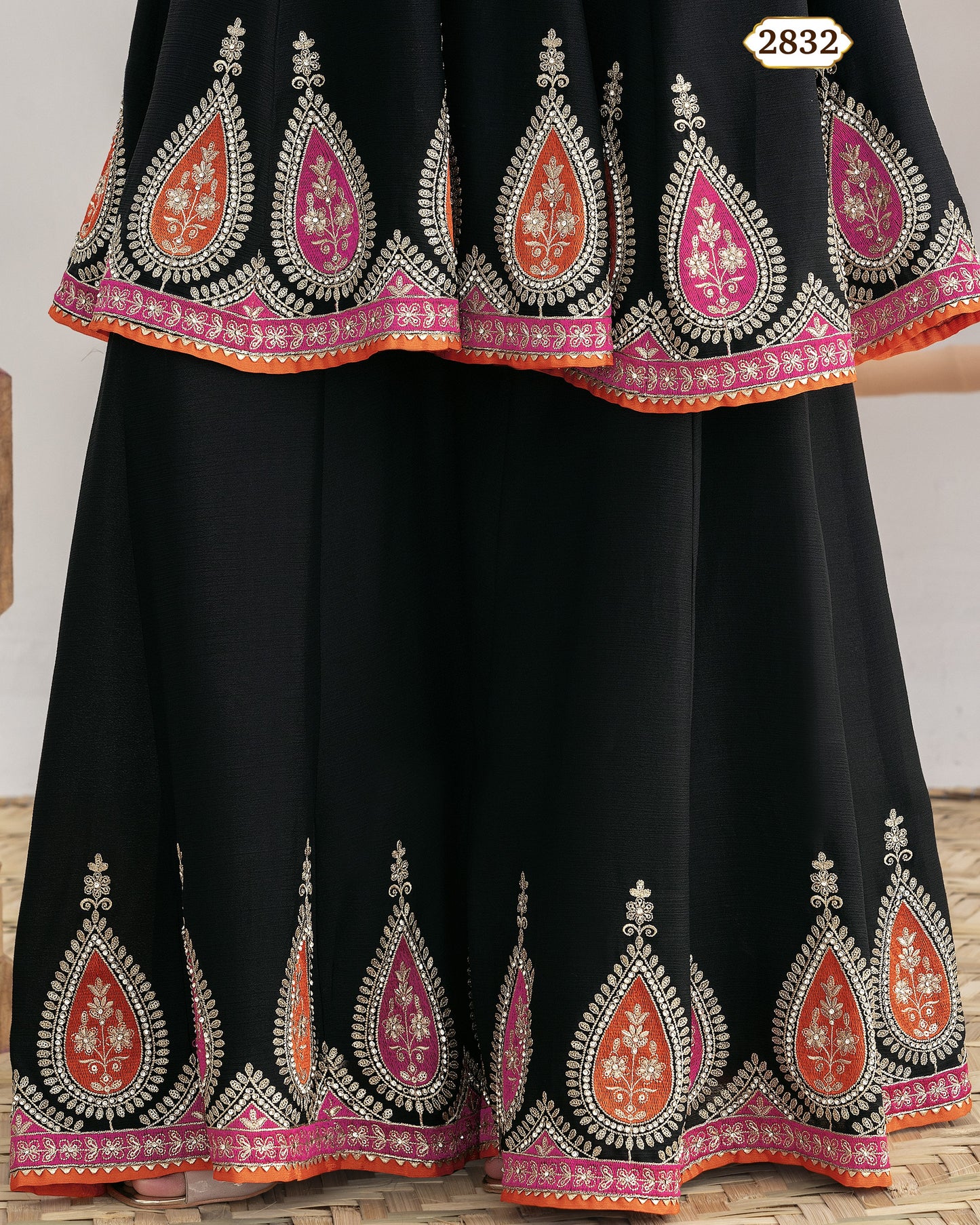 Black traditional outfit with intricate red and pink embroidery on a wooden floor.
