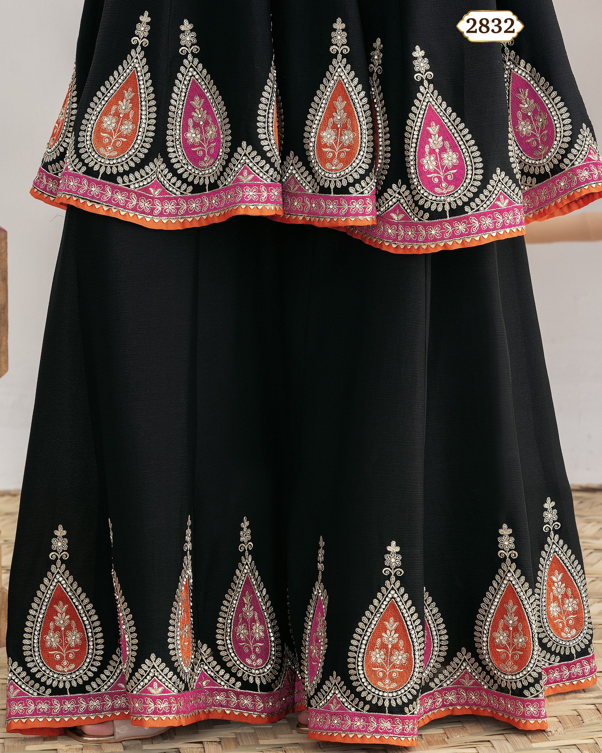 Black traditional outfit with intricate red and pink embroidery on a wooden floor.