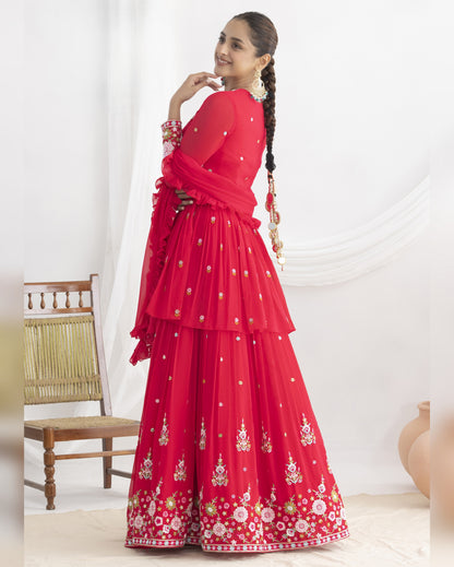 Woman in a red traditional outfit with floral patterns standing against a white background
