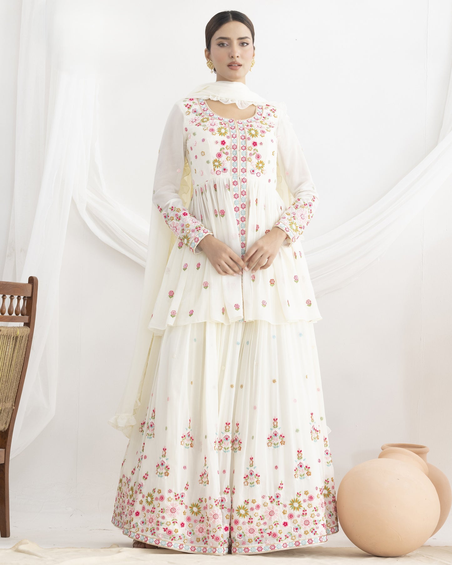 Woman wearing a white floral dress with a sheer dupatta against a white background