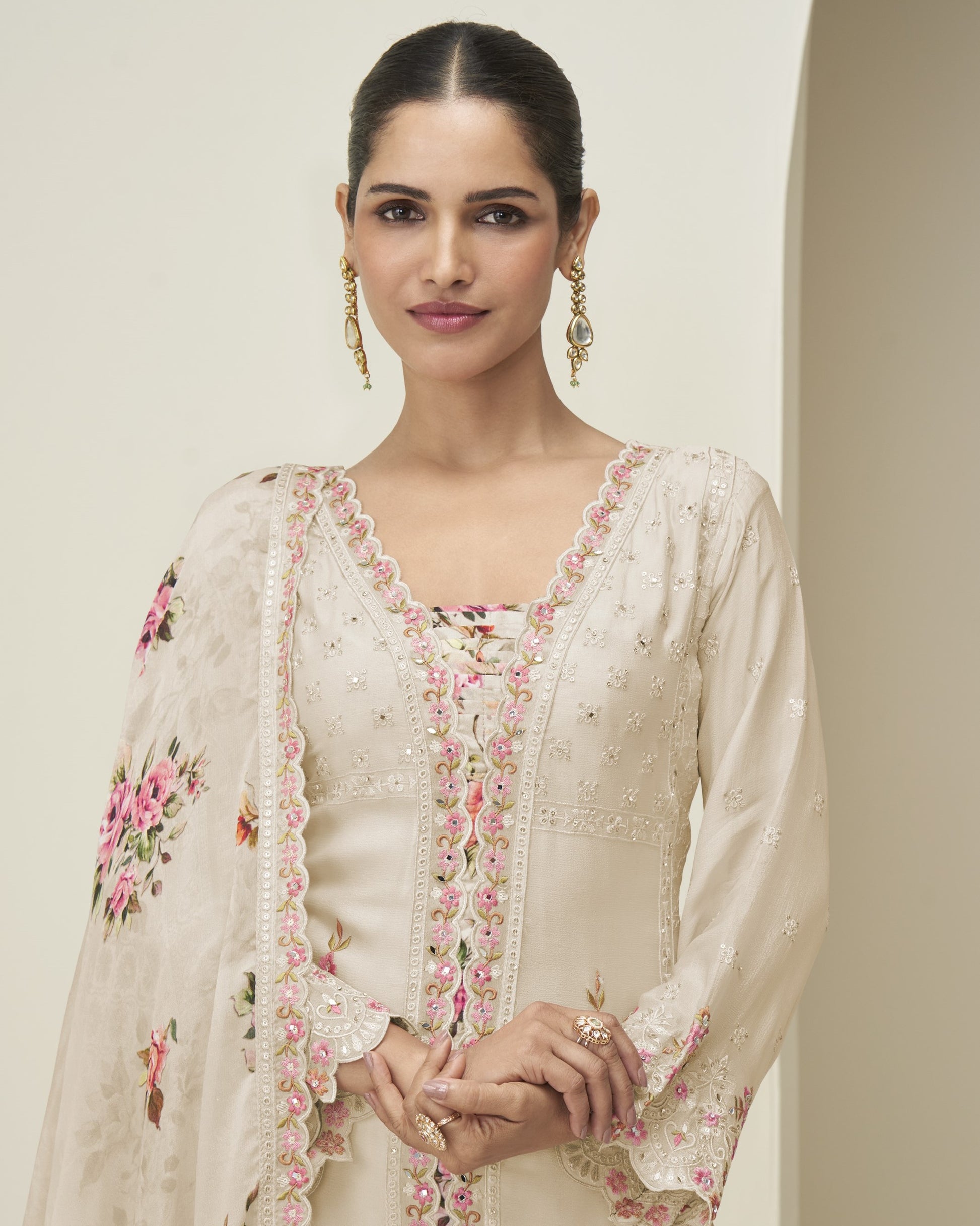 Woman wearing a cream-colored embroidered traditional outfit with floral patterns on a plain background