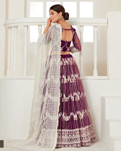 Woman in a purple and white traditional outfit standing in a bright room.