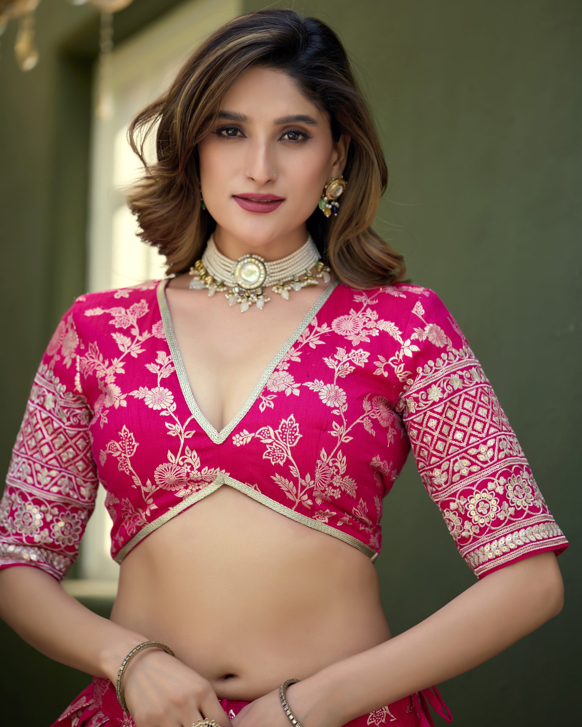 Woman wearing a pink and white traditional outfit with gold jewelry against a neutral background