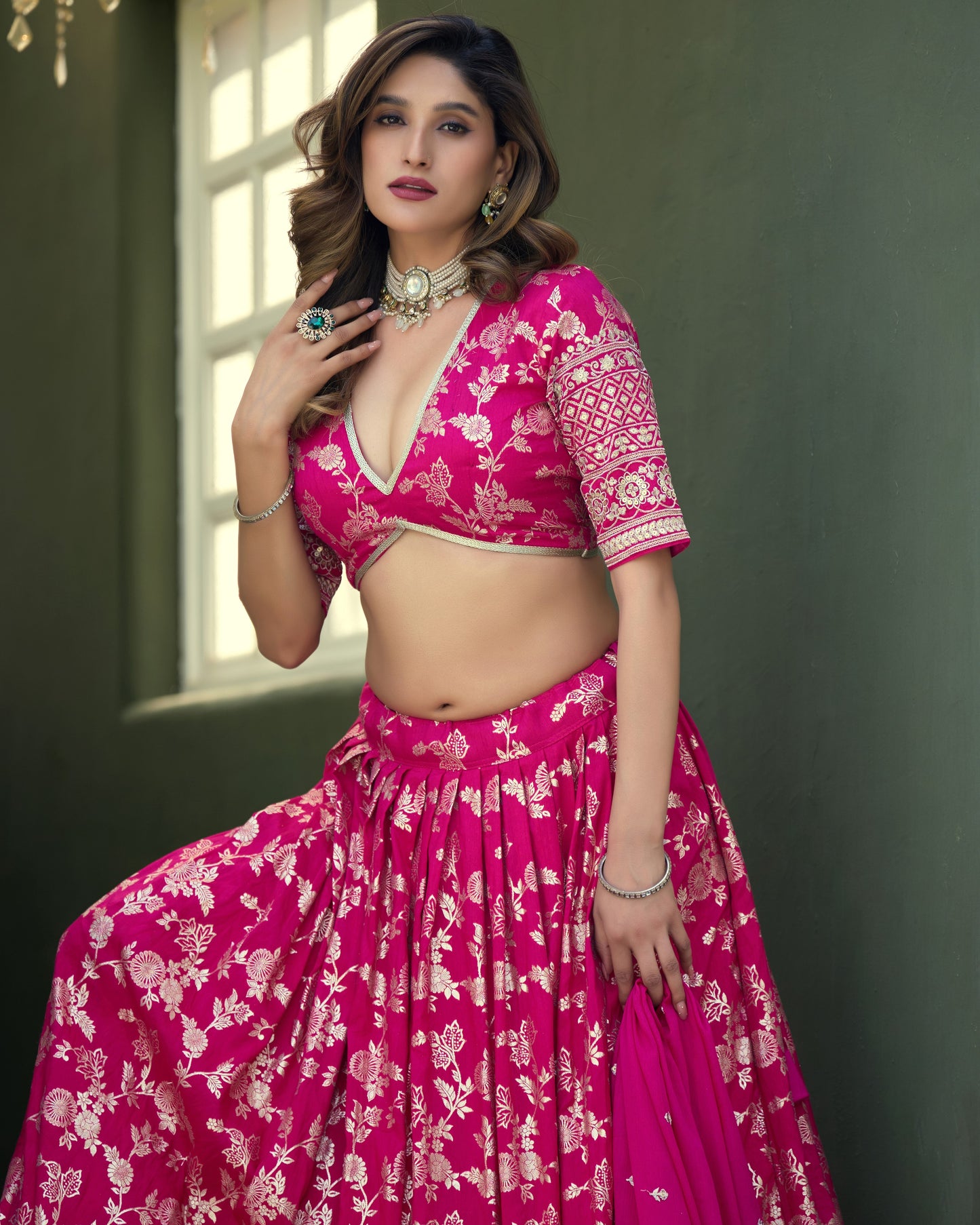 Woman wearing a pink traditional outfit with floral patterns against a green wall.