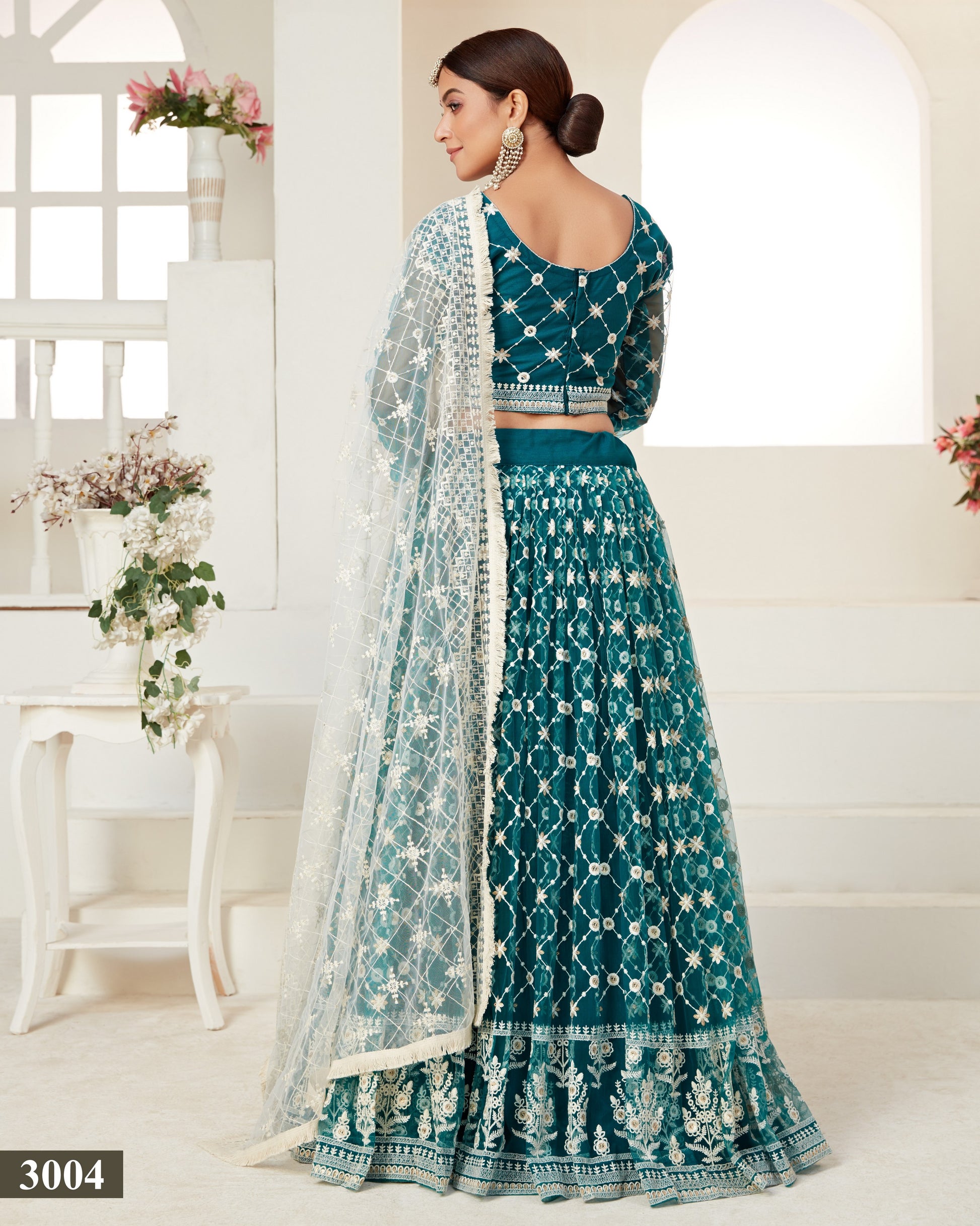 Teal embroidered lehenga with matching blouse in a bright room.