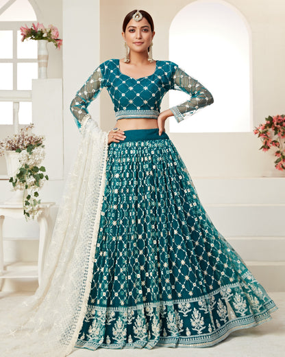 Woman wearing a teal traditional outfit with white patterns in a bright room.