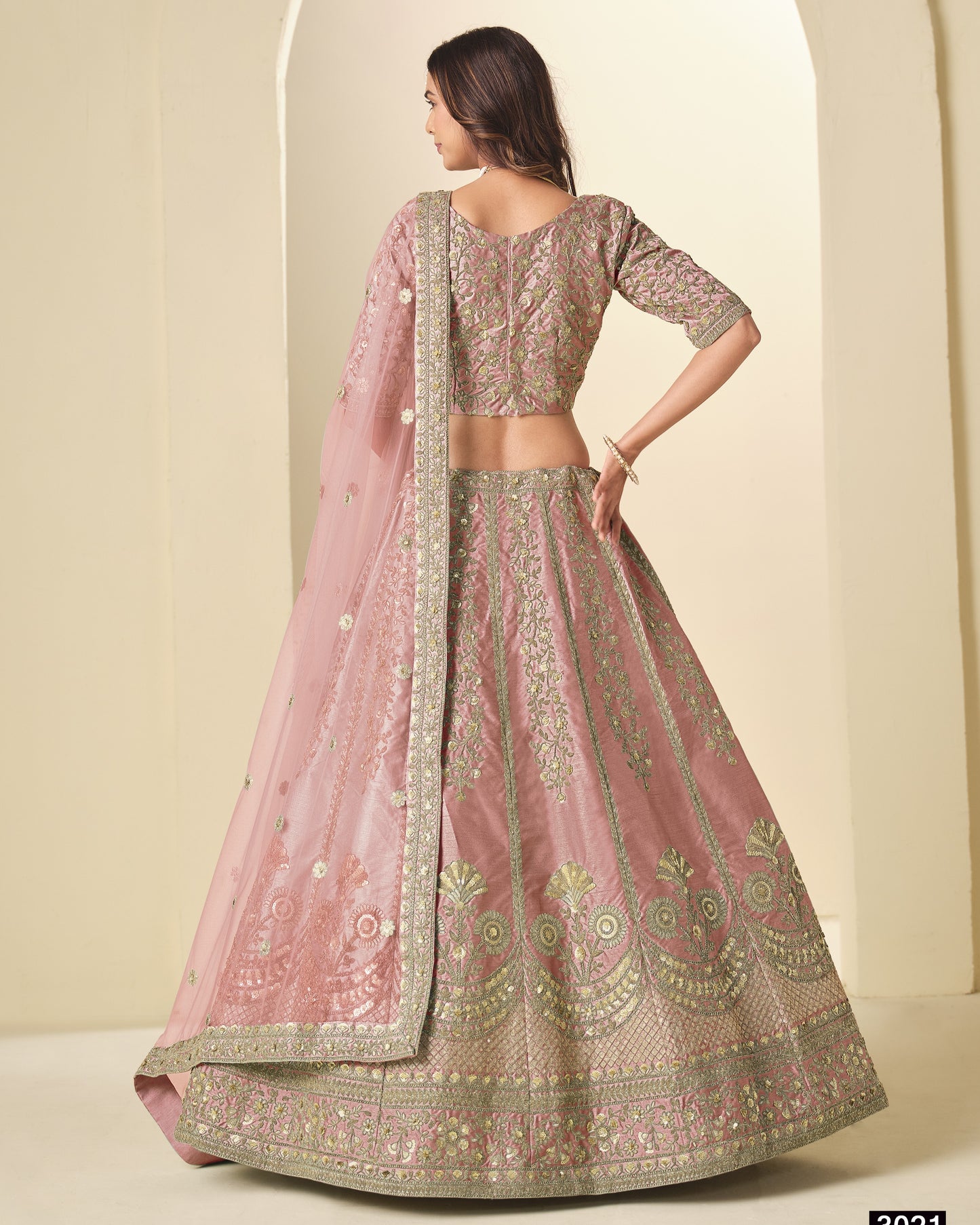 Woman wearing a traditional pink and gold embroidered lehenga with a matching dupatta.