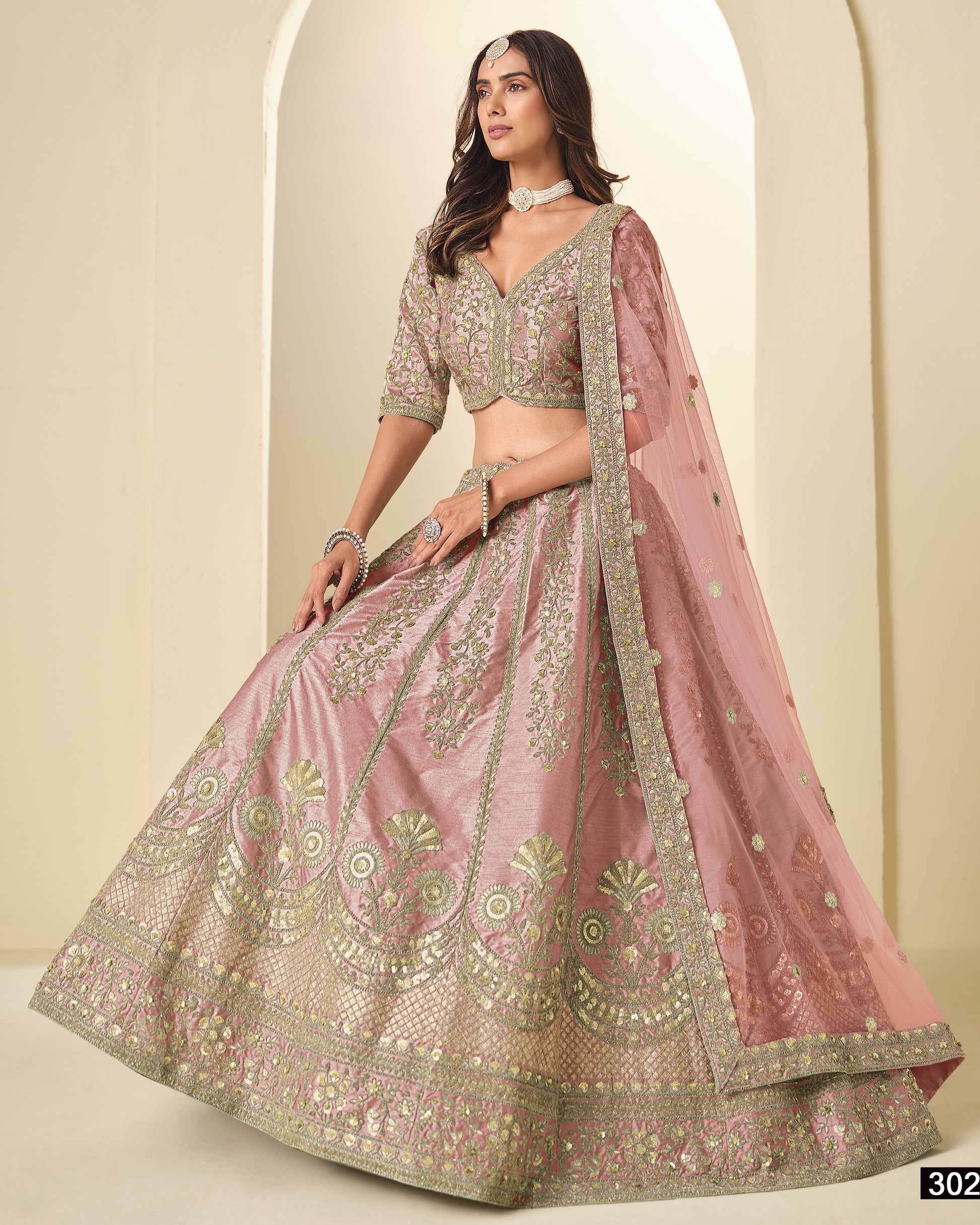Woman wearing a traditional pink and green embroidered lehenga with a plain background
