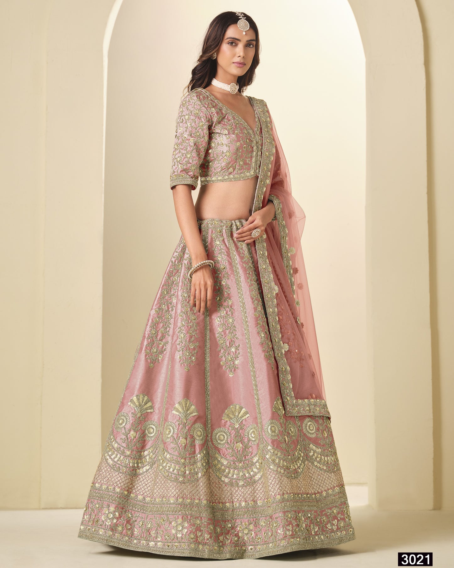 Woman wearing a traditional embroidered pink and gold lehenga against a neutral background