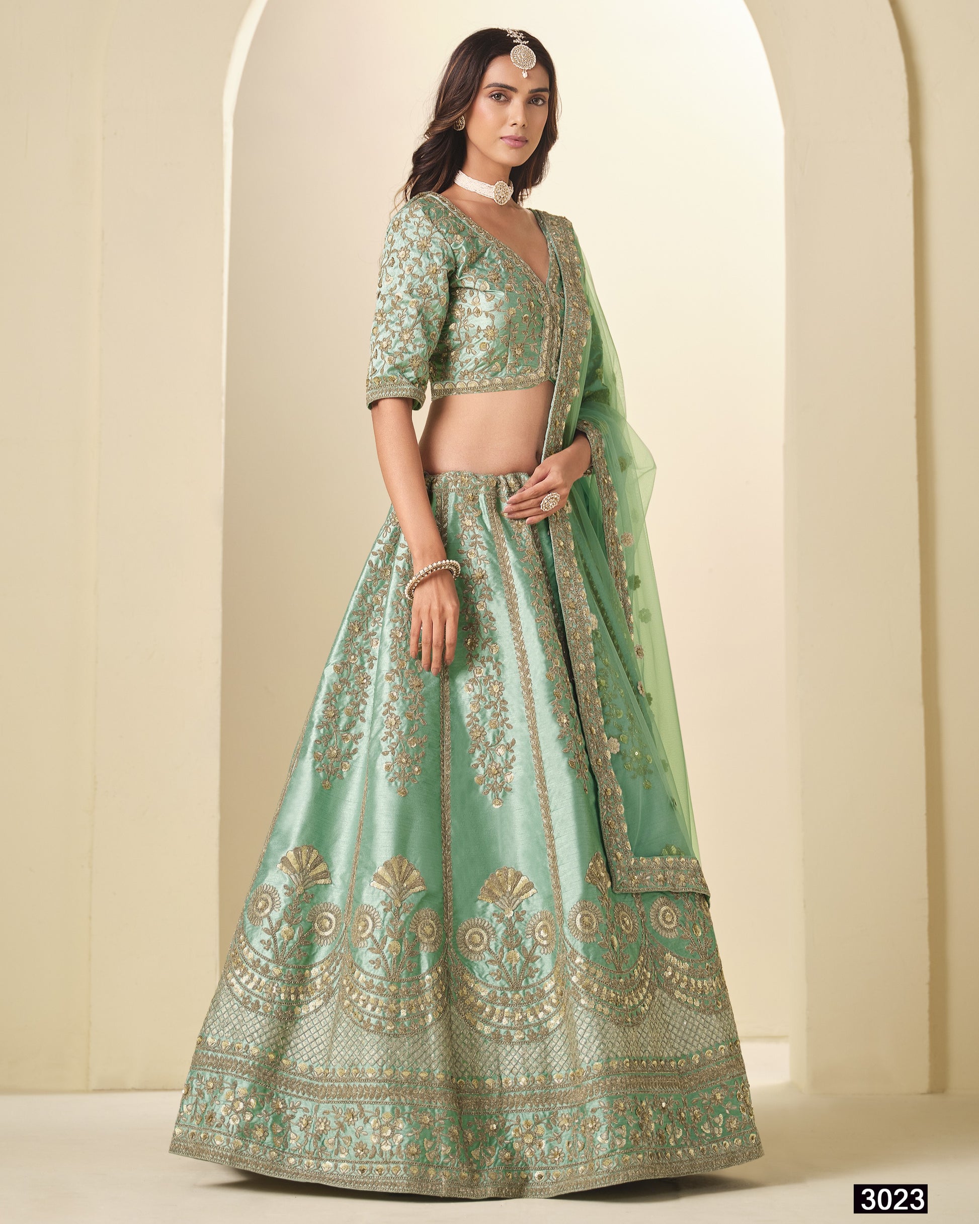 Woman wearing a green embroidered traditional outfit against a neutral background
