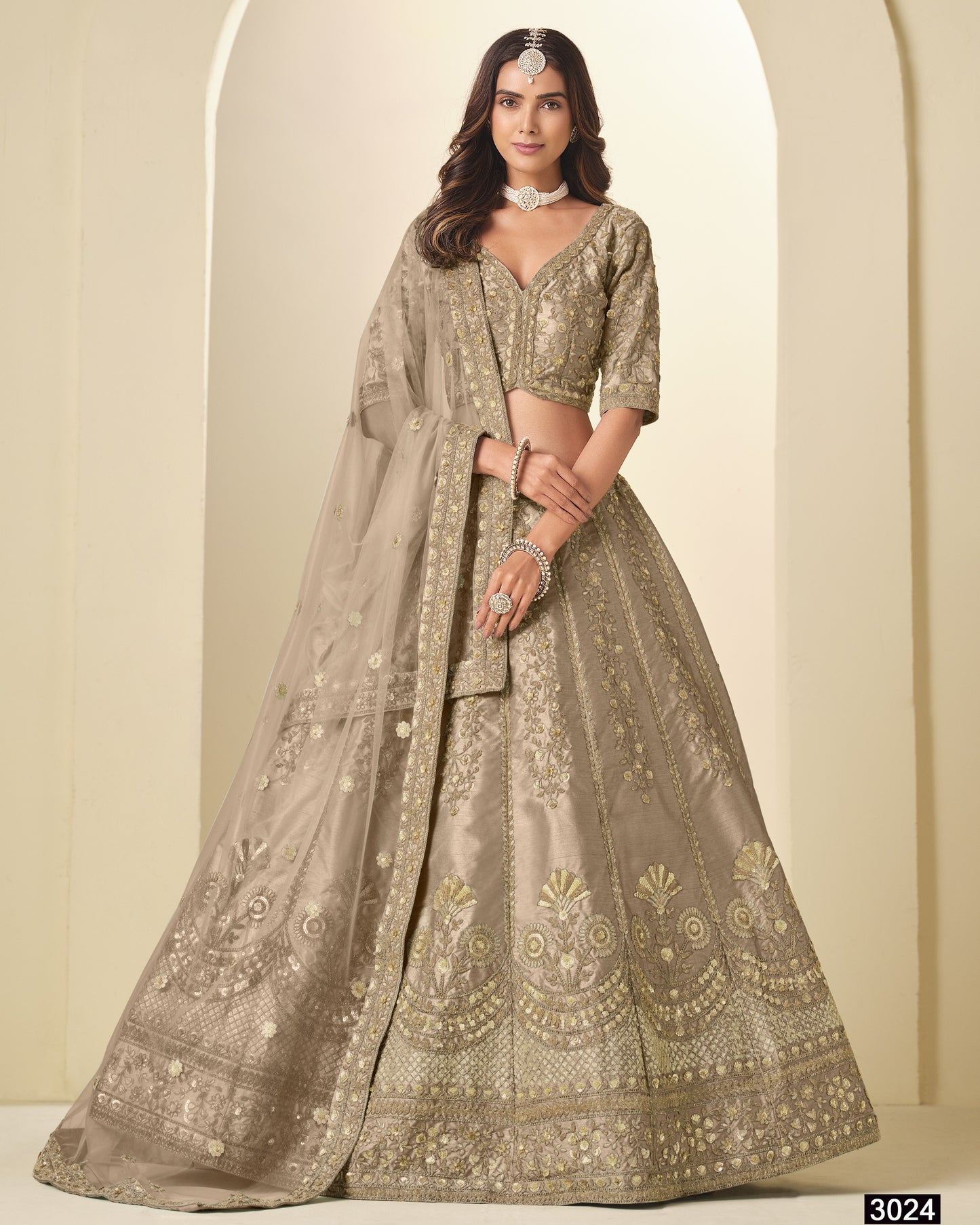 Woman wearing a traditional embroidered lehenga with a plain background