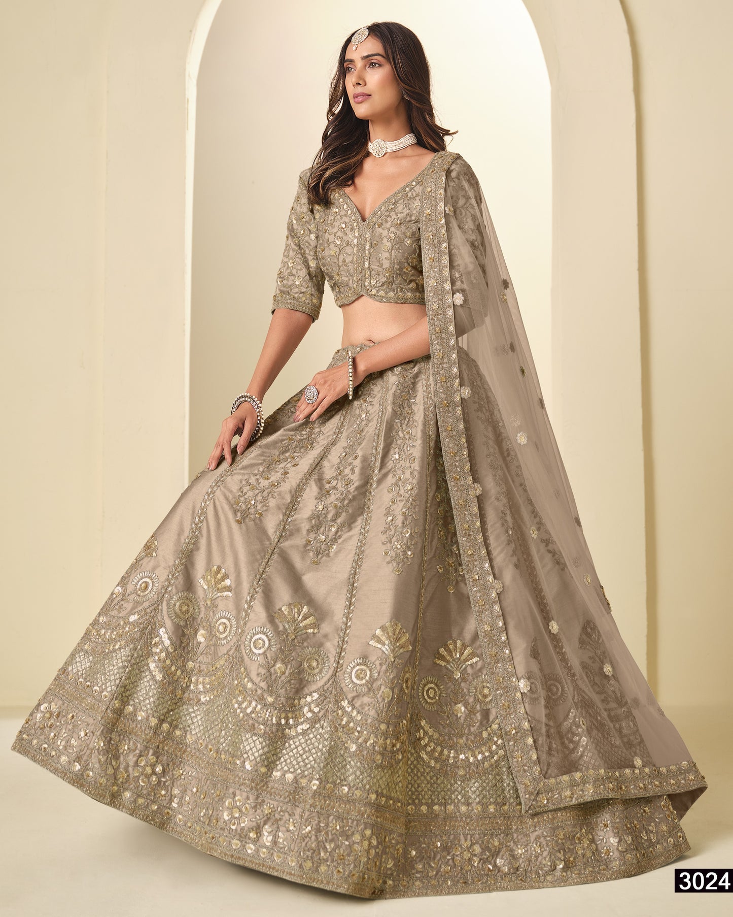 Woman wearing a traditional embroidered lehenga with a plain background