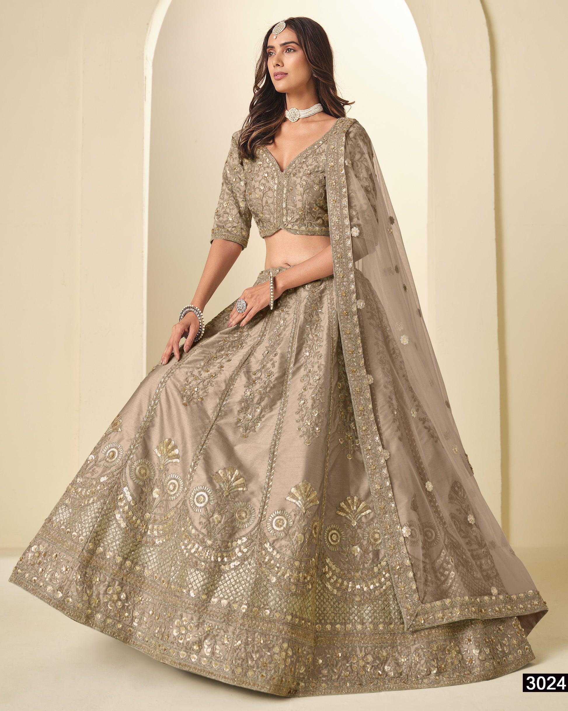 Woman wearing a traditional embroidered lehenga with a plain background