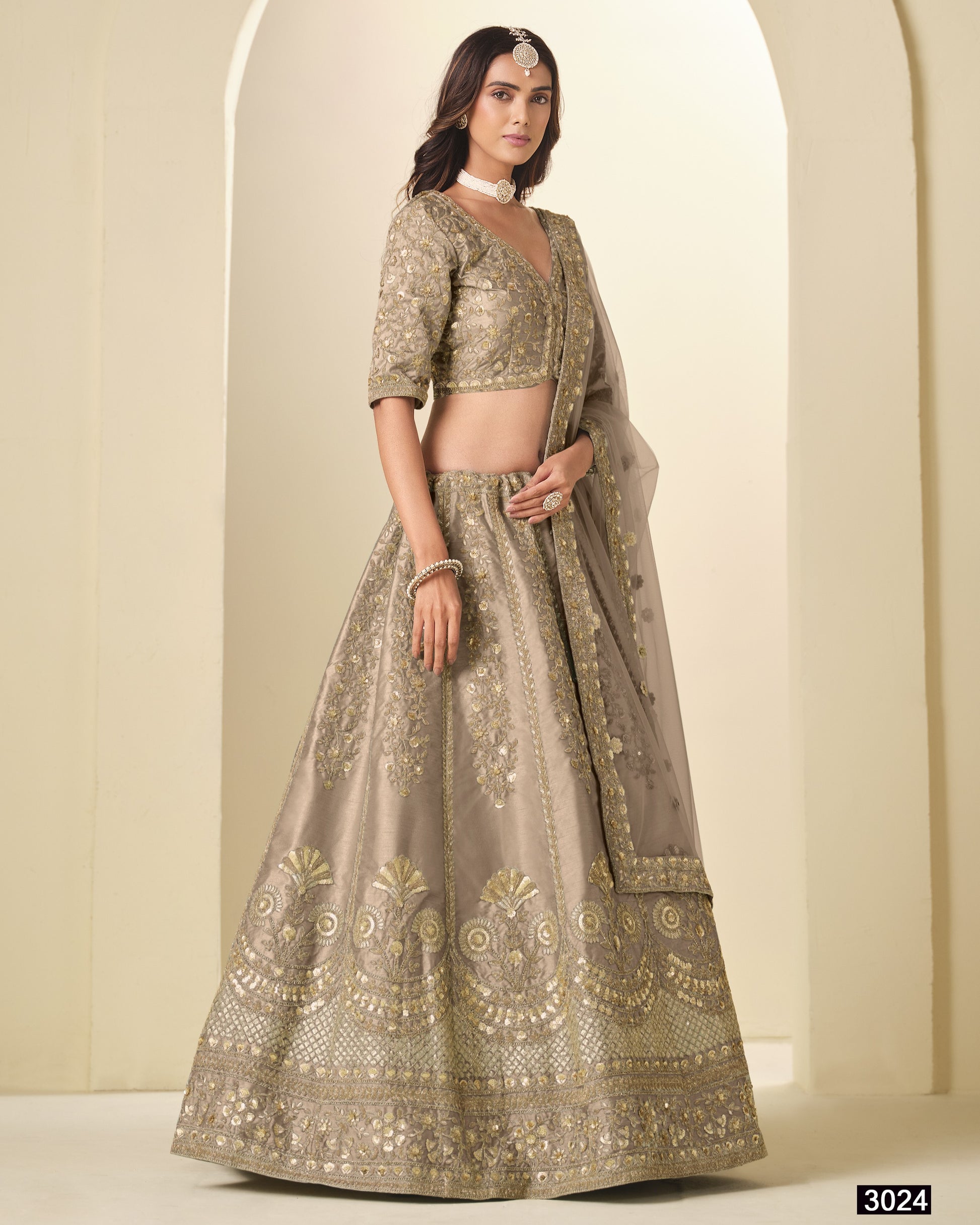 Woman wearing a traditional embroidered lehenga with a plain background