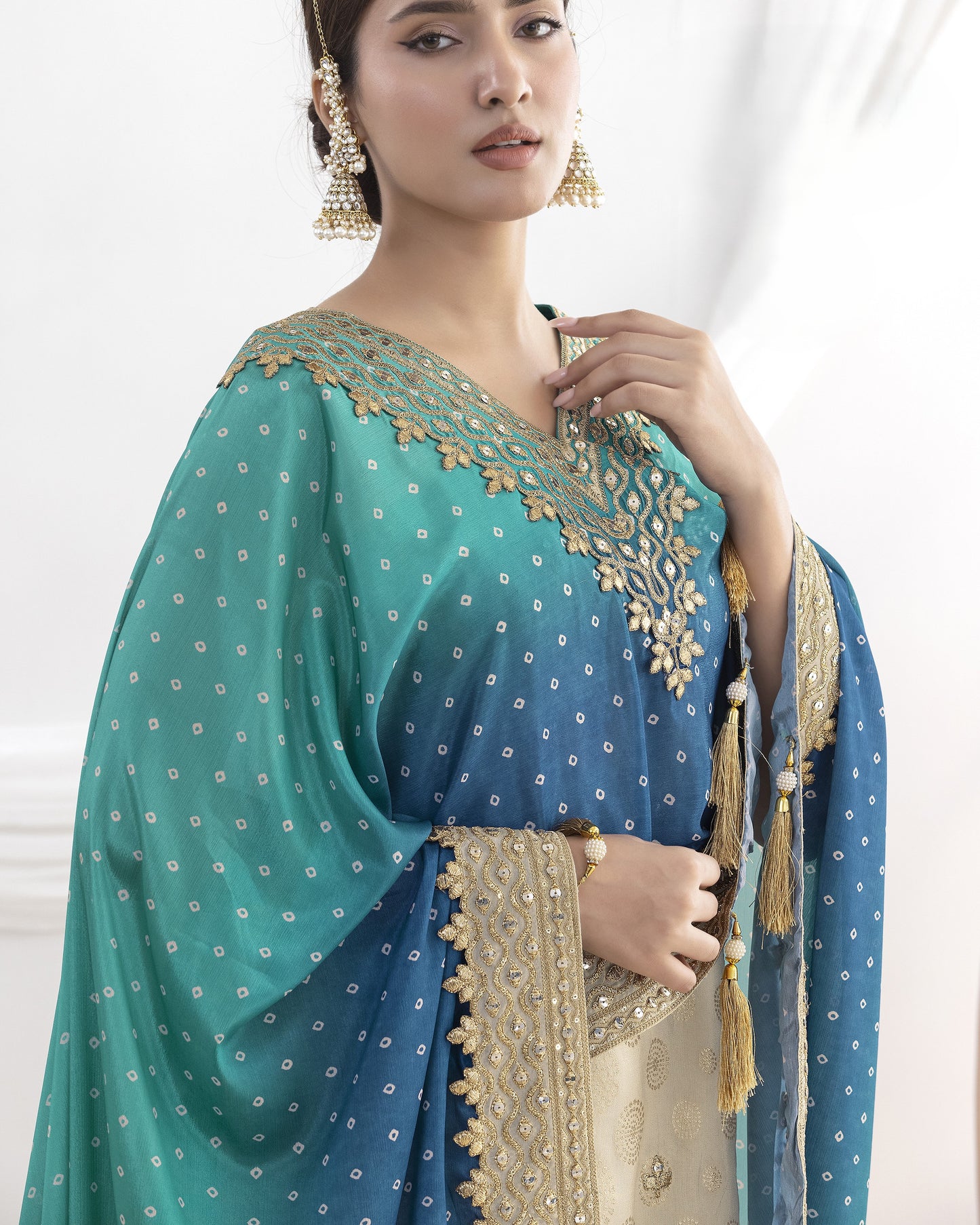 Woman wearing a traditional blue and green saree with gold embroidery on a white background