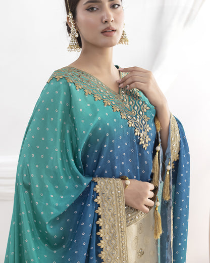 Woman wearing a traditional blue and green saree with gold embroidery on a white background