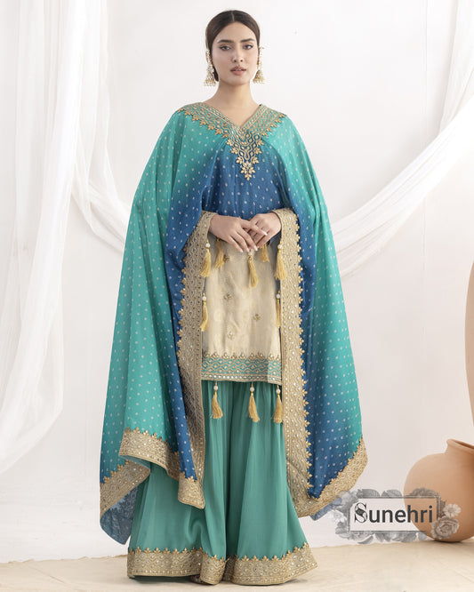 Woman wearing a teal and blue traditional outfit with gold embroidery against a white background