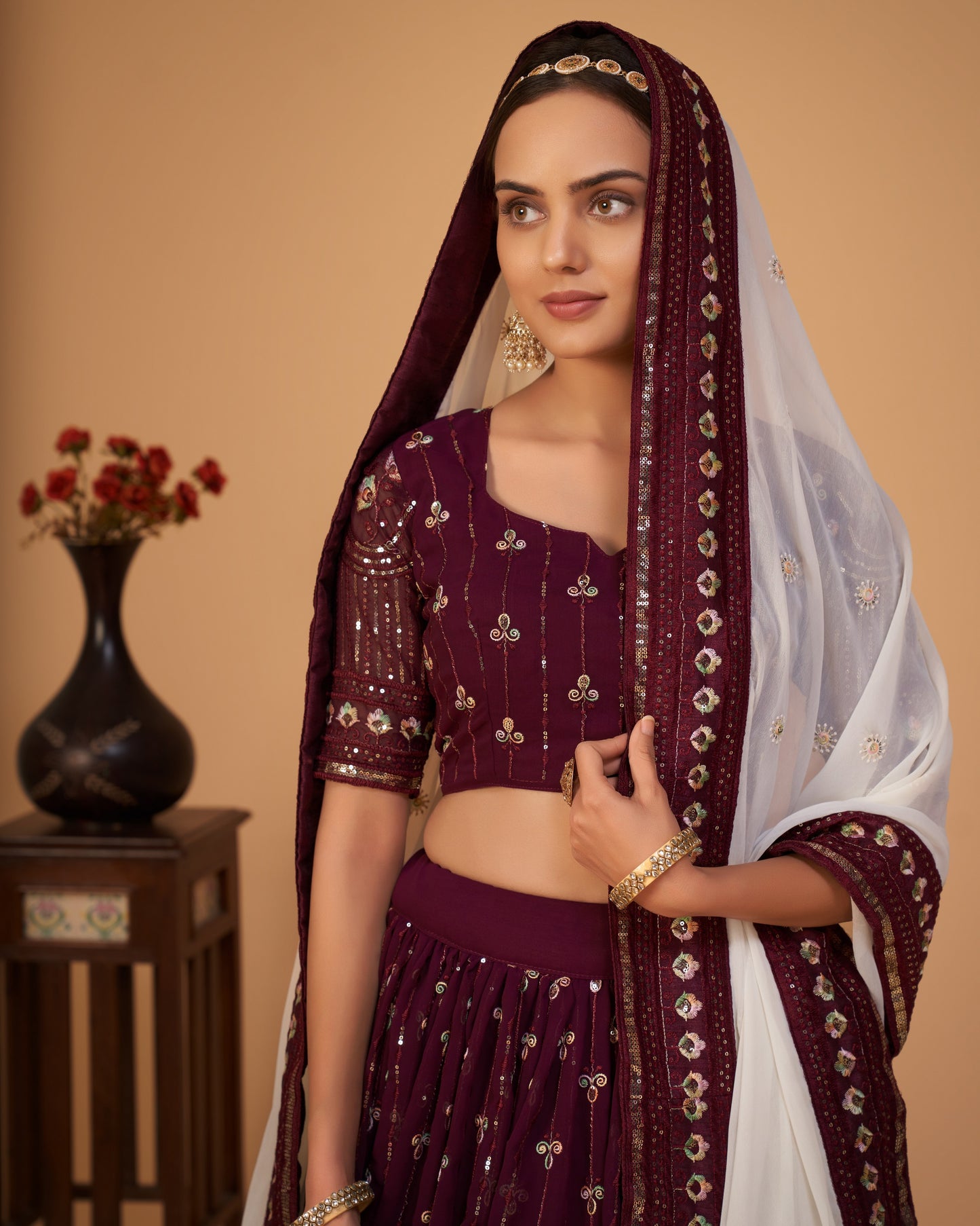 Woman wearing a traditional maroon and white outfit with a matching dupatta against a beige background.