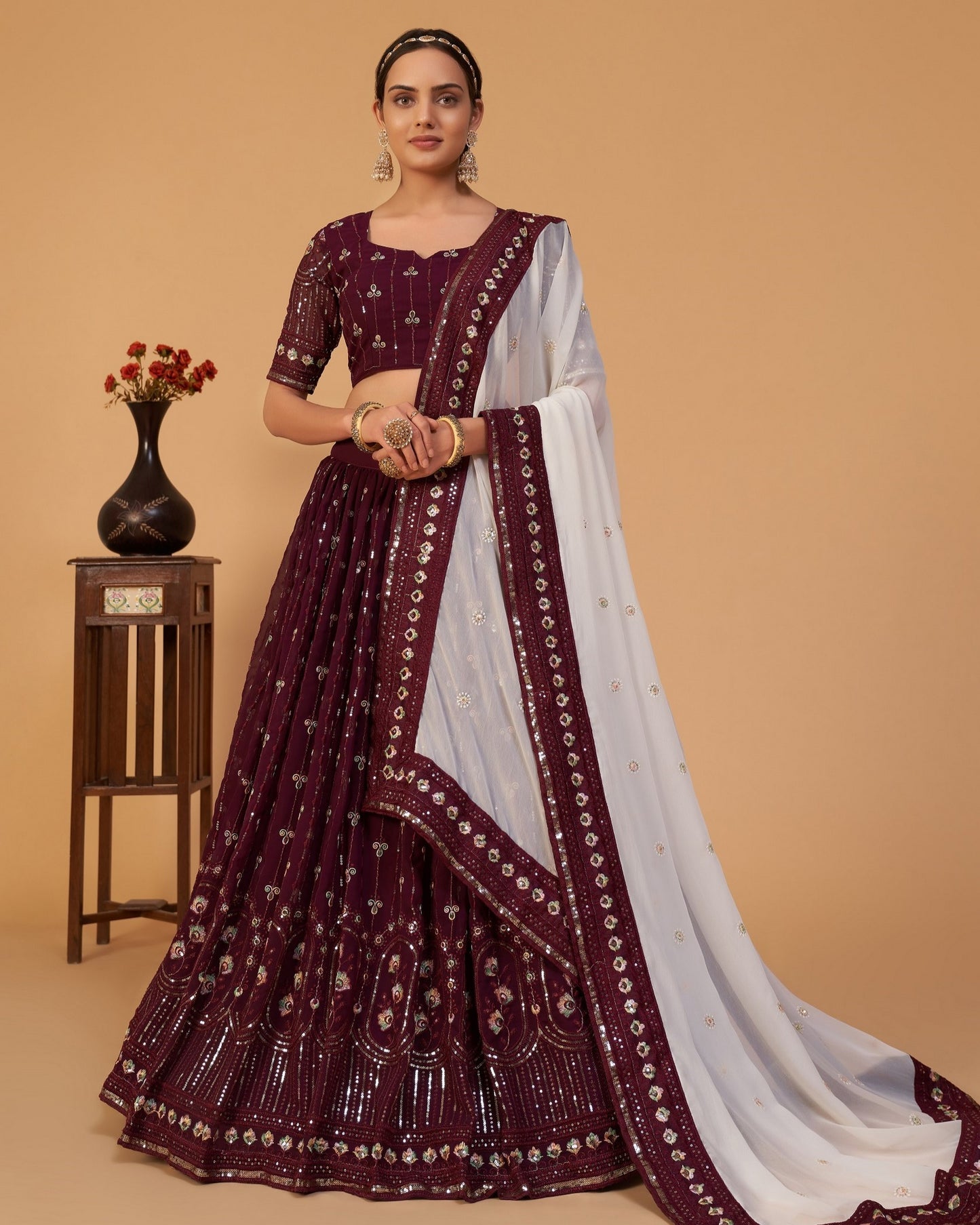 Woman wearing a maroon and white saree with intricate patterns on a beige background