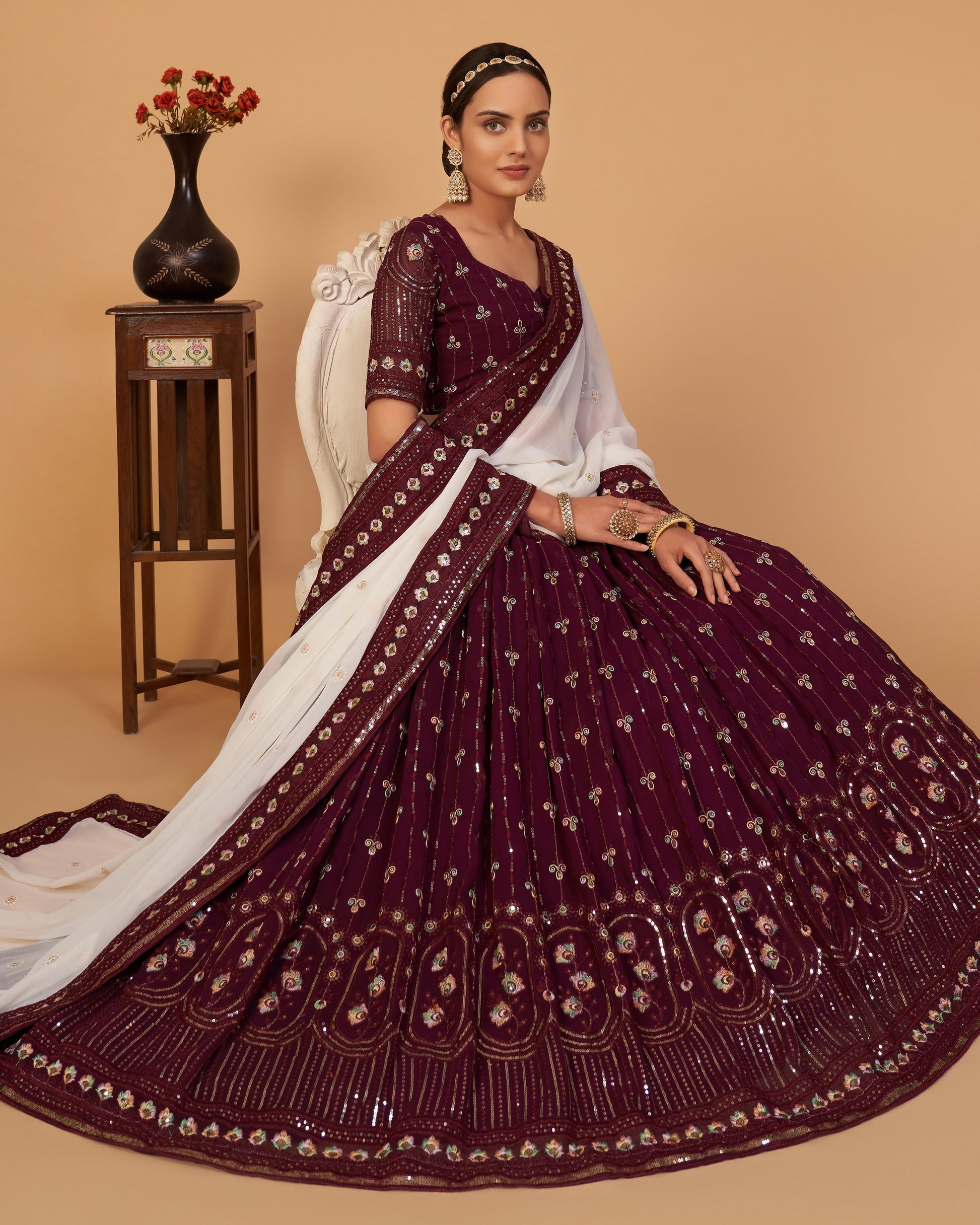 Woman wearing a maroon and white saree with intricate patterns on a beige background