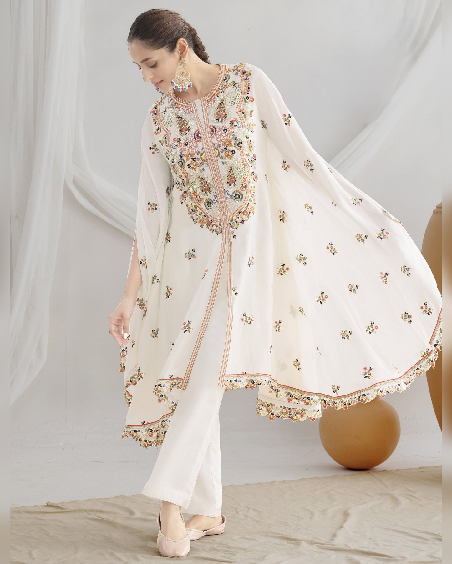 Woman wearing a white embroidered outfit with a sheer dupatta against a neutral background