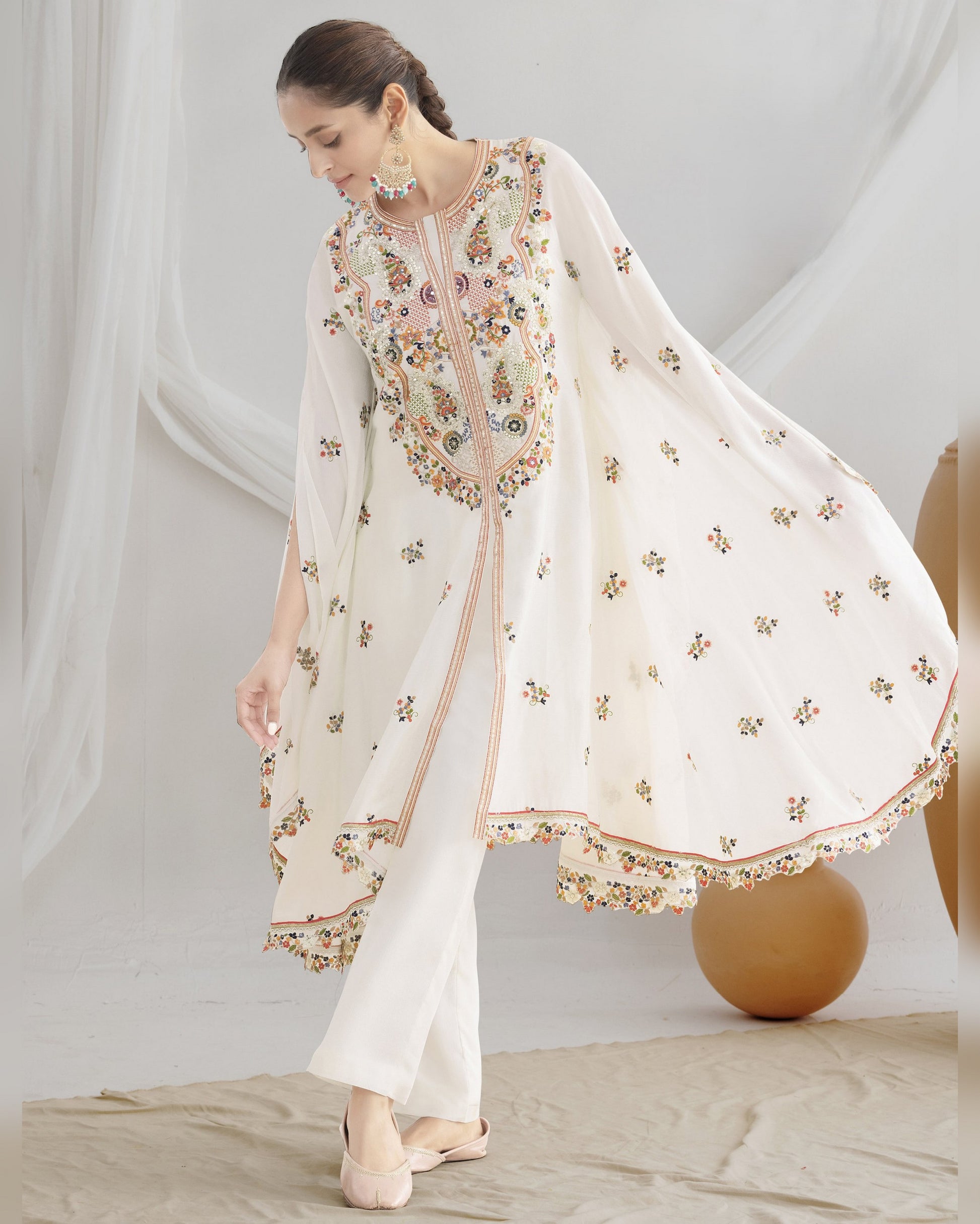 Woman wearing a white embroidered outfit with a sheer dupatta against a neutral background
