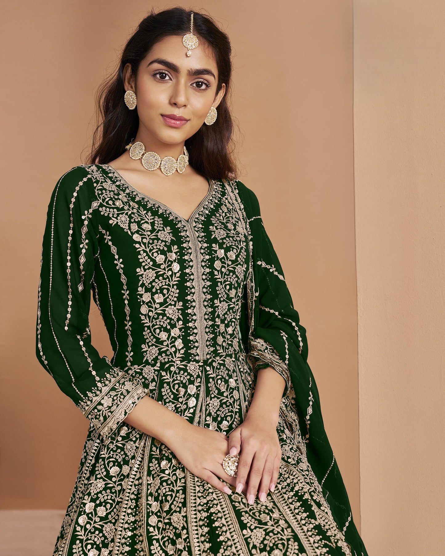 Woman wearing a green and gold traditional outfit with jewelry against a beige background