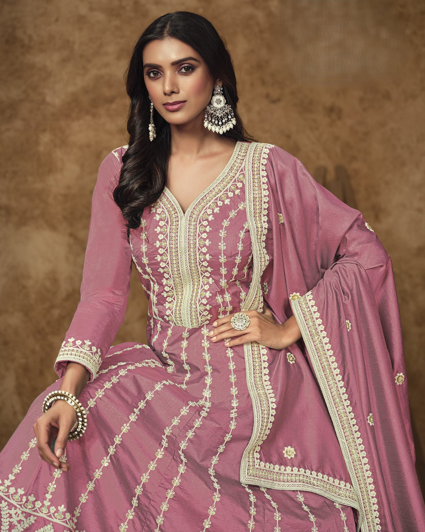 Woman wearing a pink traditional outfit with intricate white embroidery against a brown background
