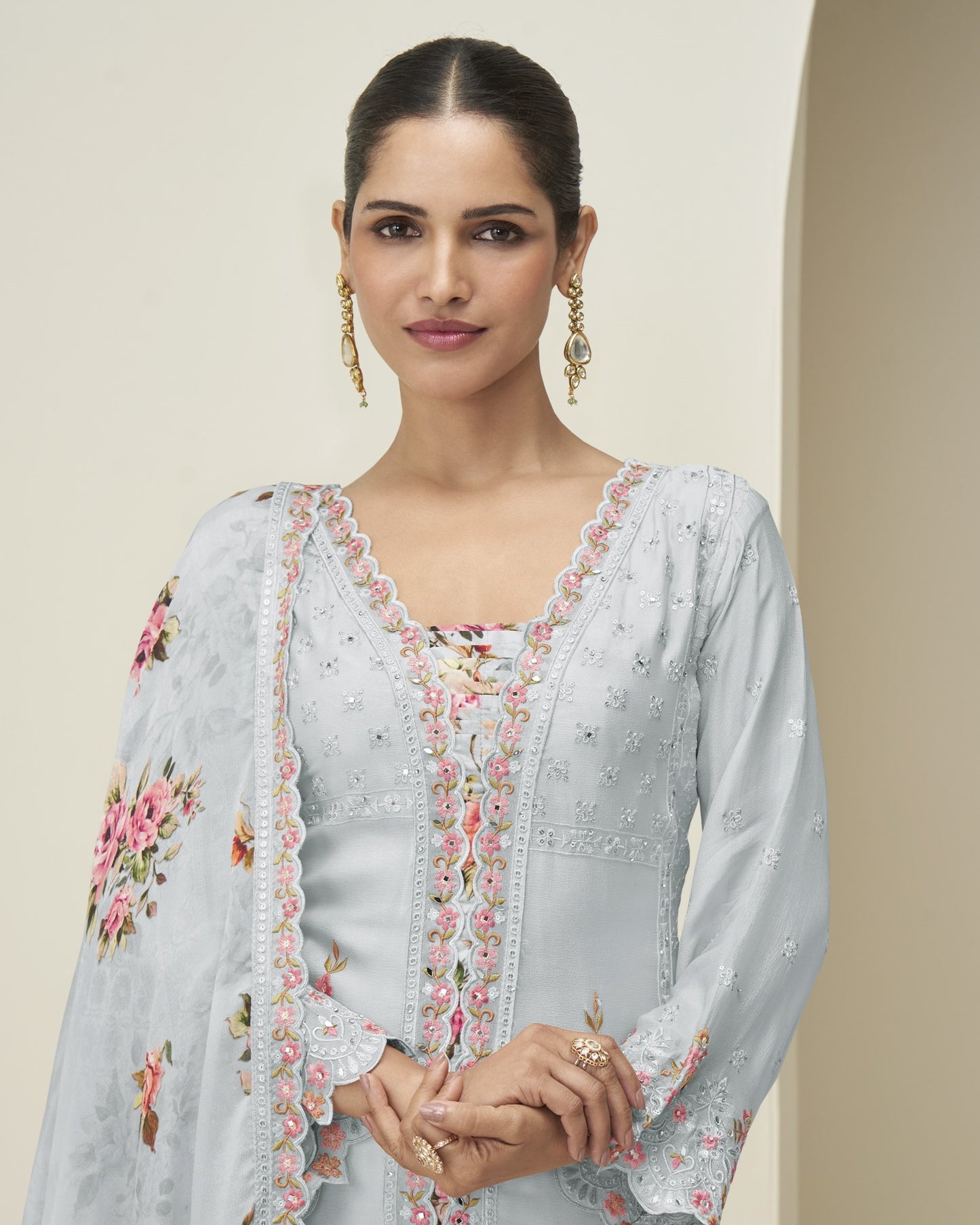 Woman wearing a light blue embroidered traditional outfit with floral patterns on a beige background