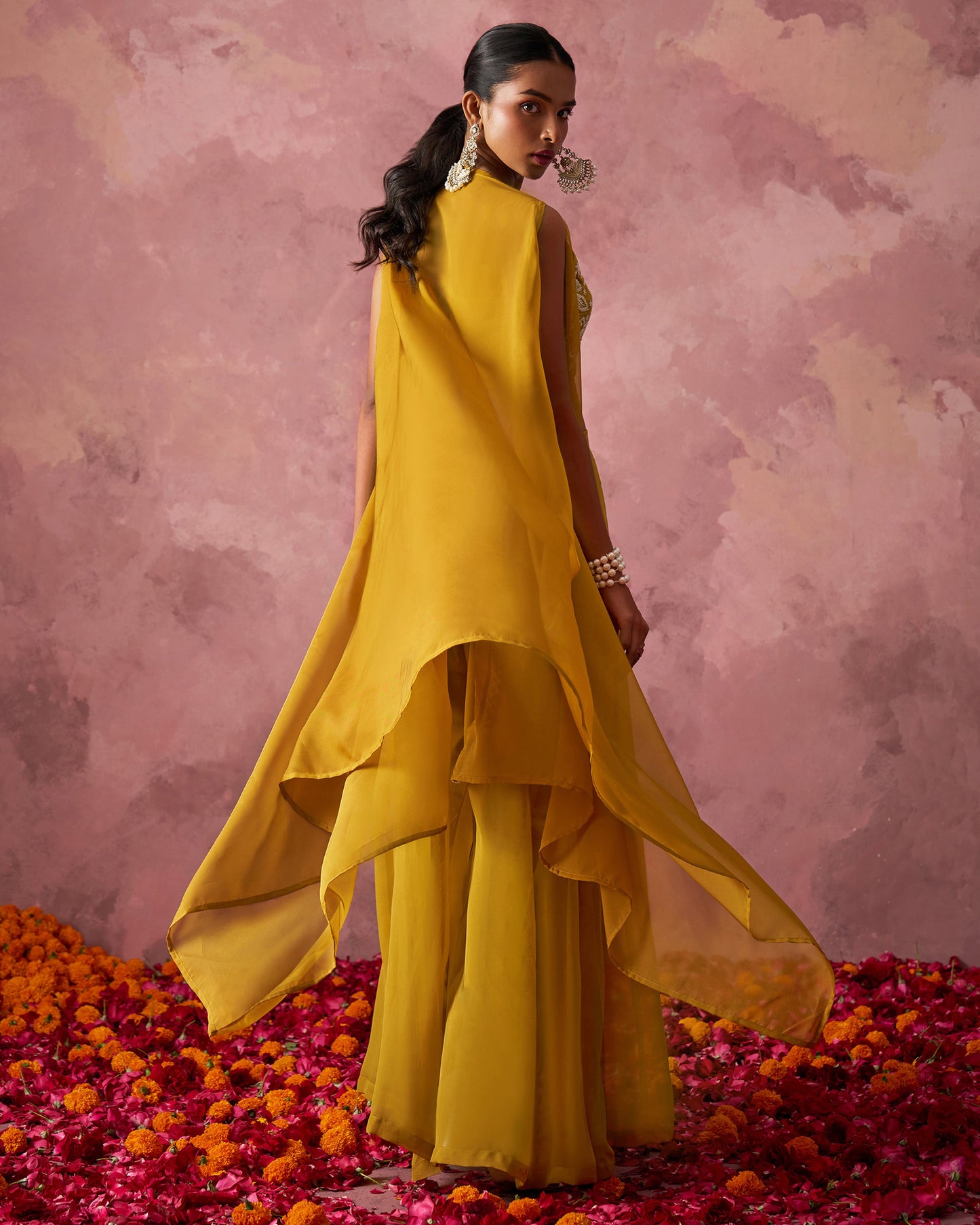 Woman in a yellow outfit standing on flower petals with a pink background