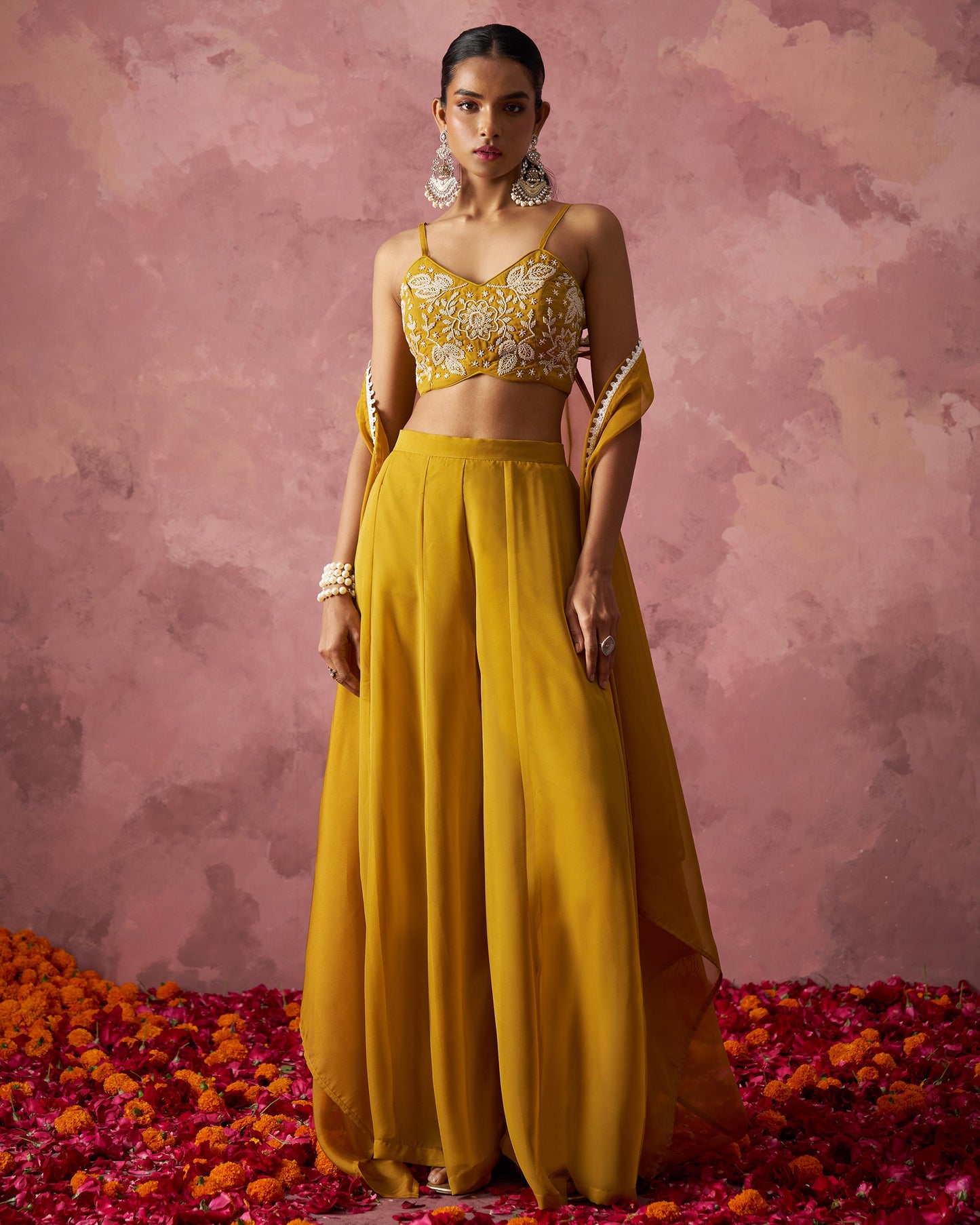 Woman in a yellow outfit with floral top and long skirt on a pink textured background with flower petals.