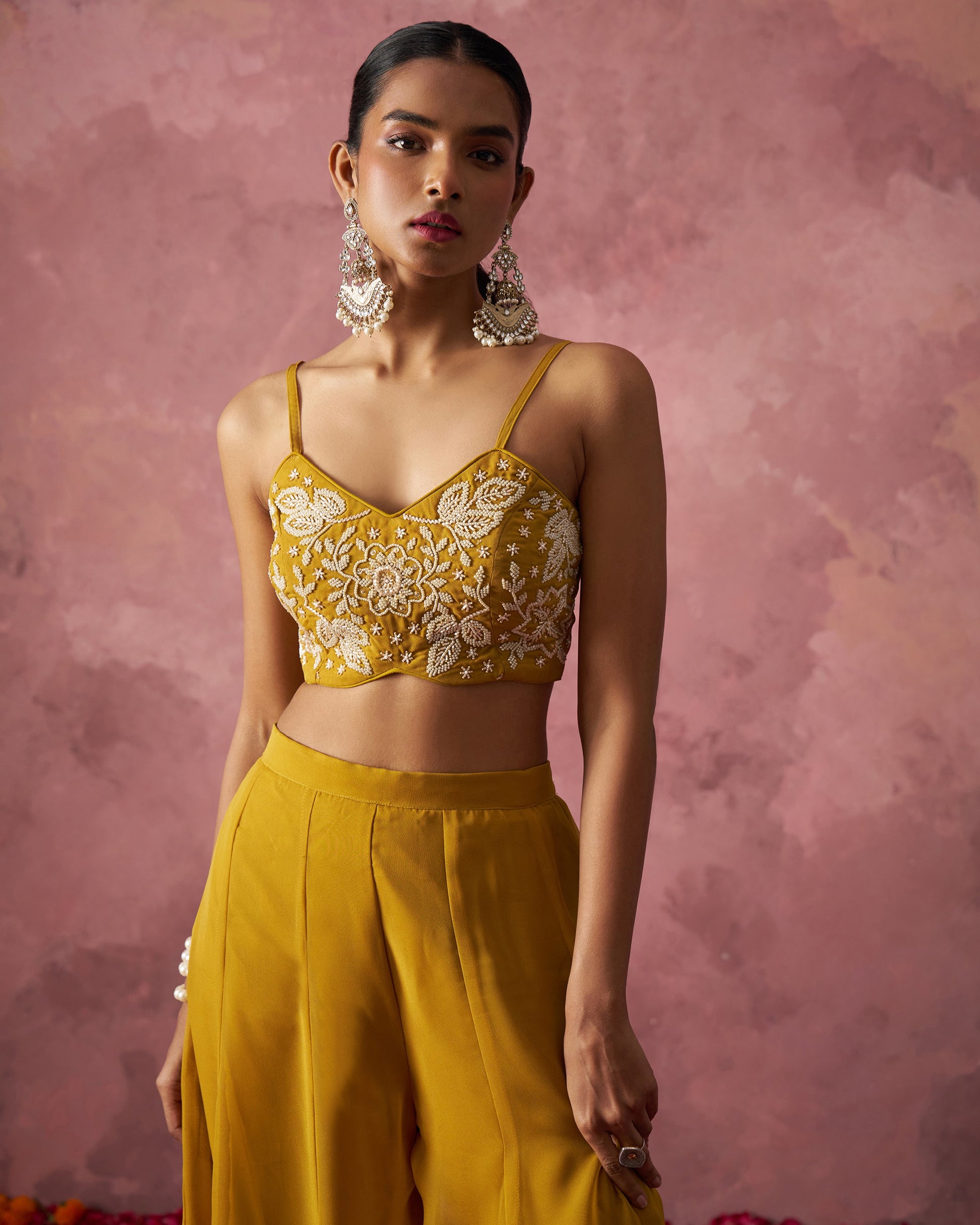 Woman wearing a yellow embroidered top and pants against a pink background