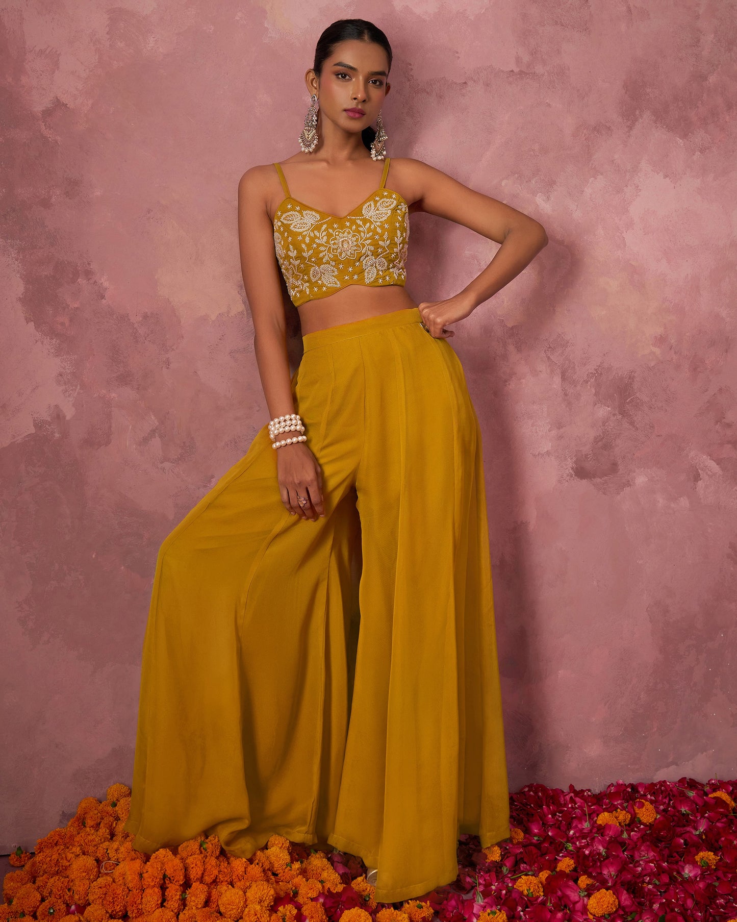 Woman in a yellow outfit with floral top and wide-leg pants standing on flowers against a pink background