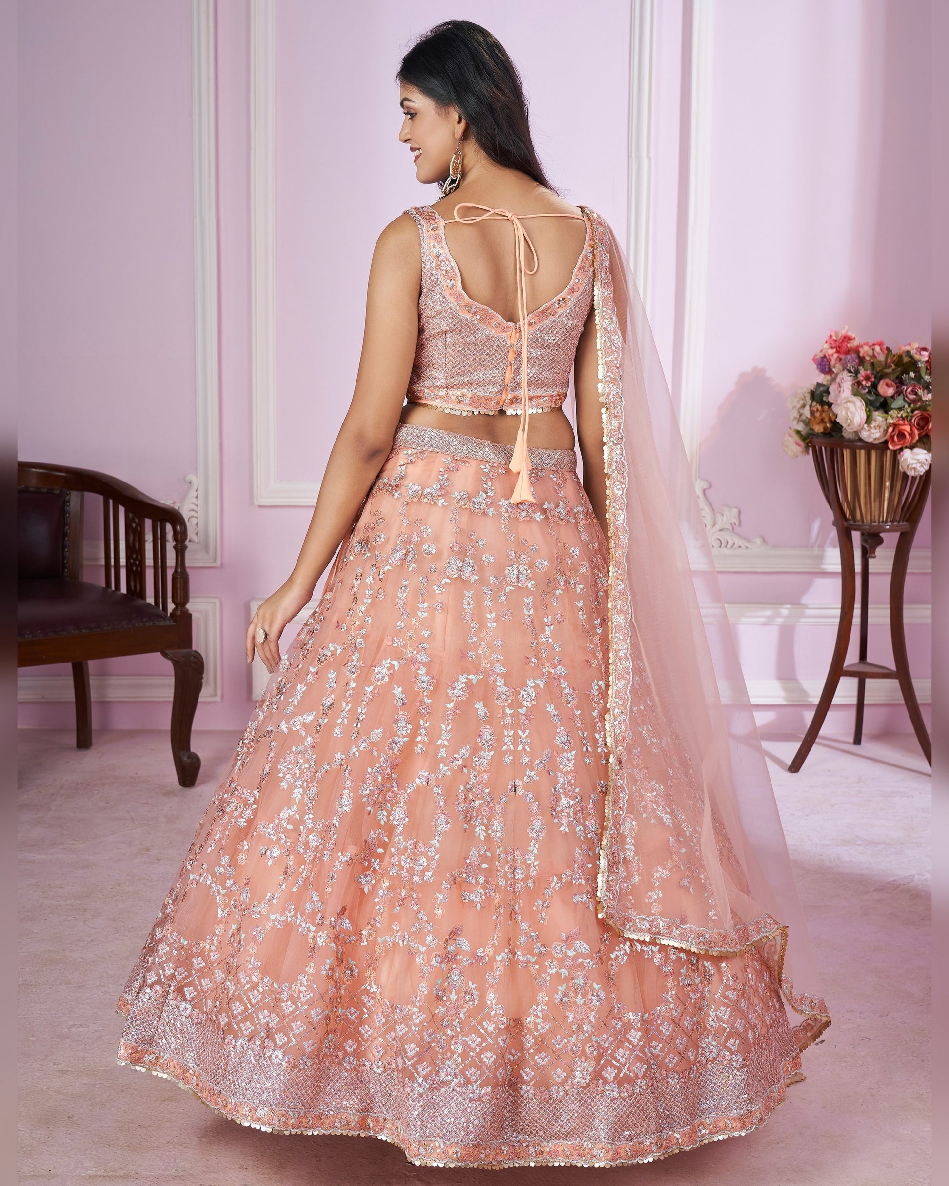 Woman wearing a peach embroidered lehenga in an elegant room setting.