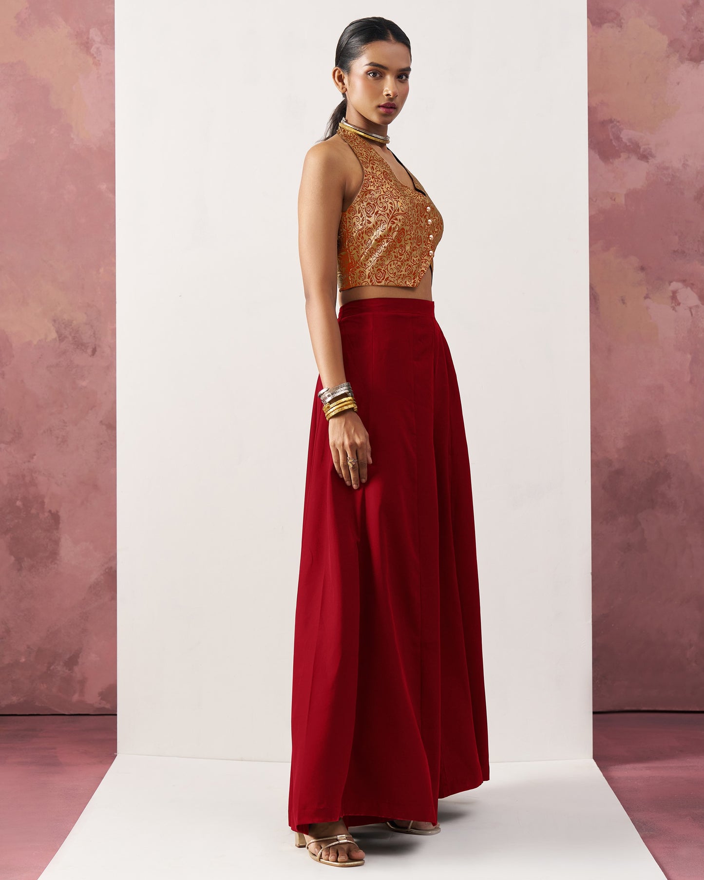 Woman wearing a gold top and red skirt against a pink and white background